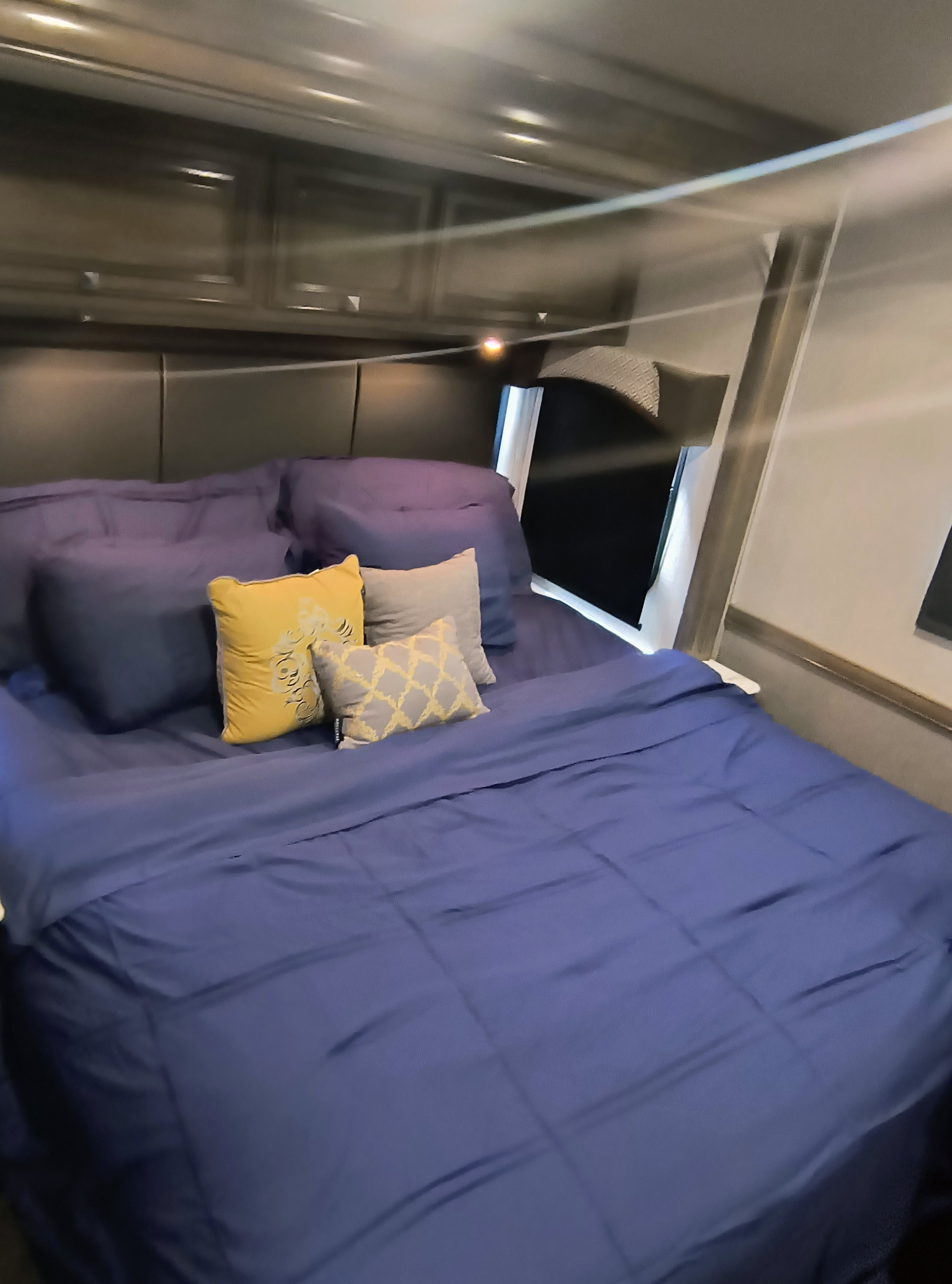 Comfortable RV rental bedroom with blue bedding, yellow accent pillows, and overhead storage for a restful trip.. Fleetwood Fortis 2020
