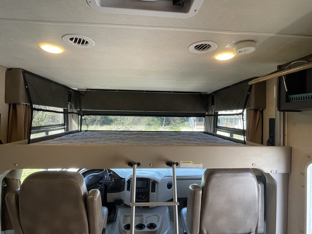 This RV rental interior showcases the cab-over bunk with a safety net, positioned above the driver's cockpit area.. Thor Freedom Traveler 2019