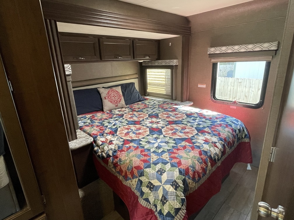 Relaxing RV rental bedroom with a comfy bed, colorful quilt, ample storage, and natural light from side windows.. Thor Freedom Traveler 2019