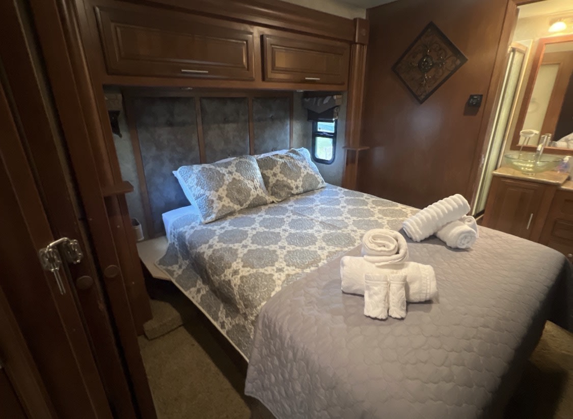 Comfortable RV rental bedroom featuring a patterned bed, fresh towels, and warm wooden interior cabinetry.. Georgetown XL 2015