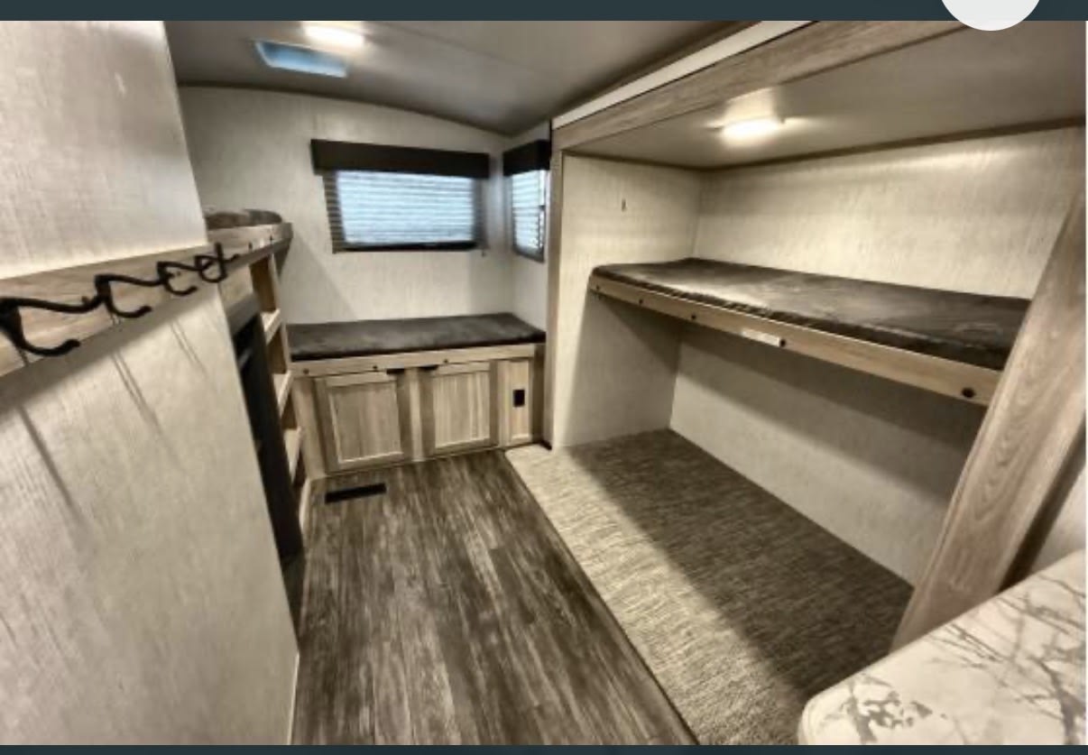 Interior of an RV rental: a cozy bunkhouse with two beds, a storage bench under windows, and coat hooks.. Cruiser RV Shadow Cruiser 2022