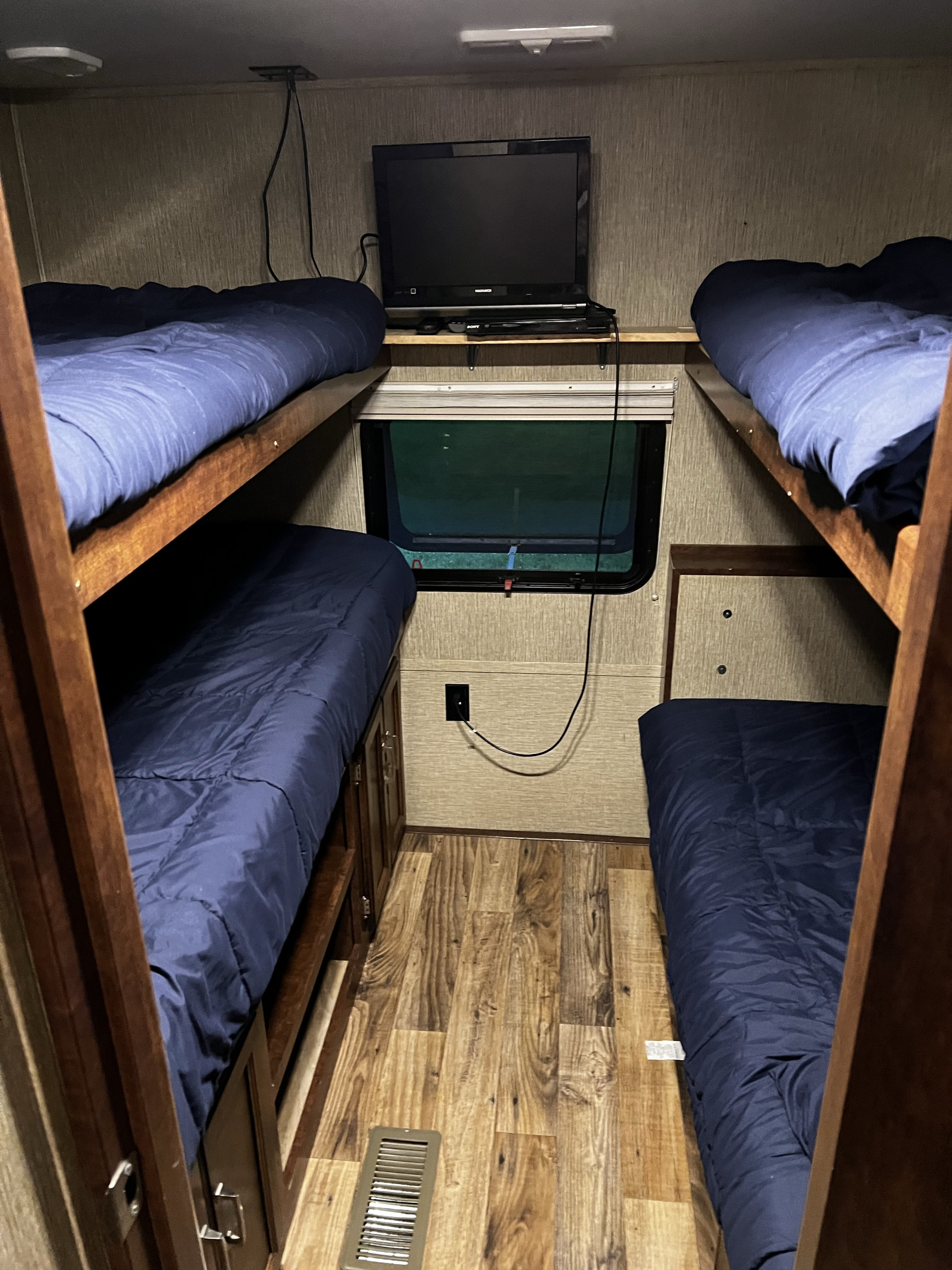 Cozy RV rental bunk room with four beds, blue bedding, a TV, a window, and wood-look flooring. Ideal for families.. Keystone RV Outback Ultra-Lite 2017