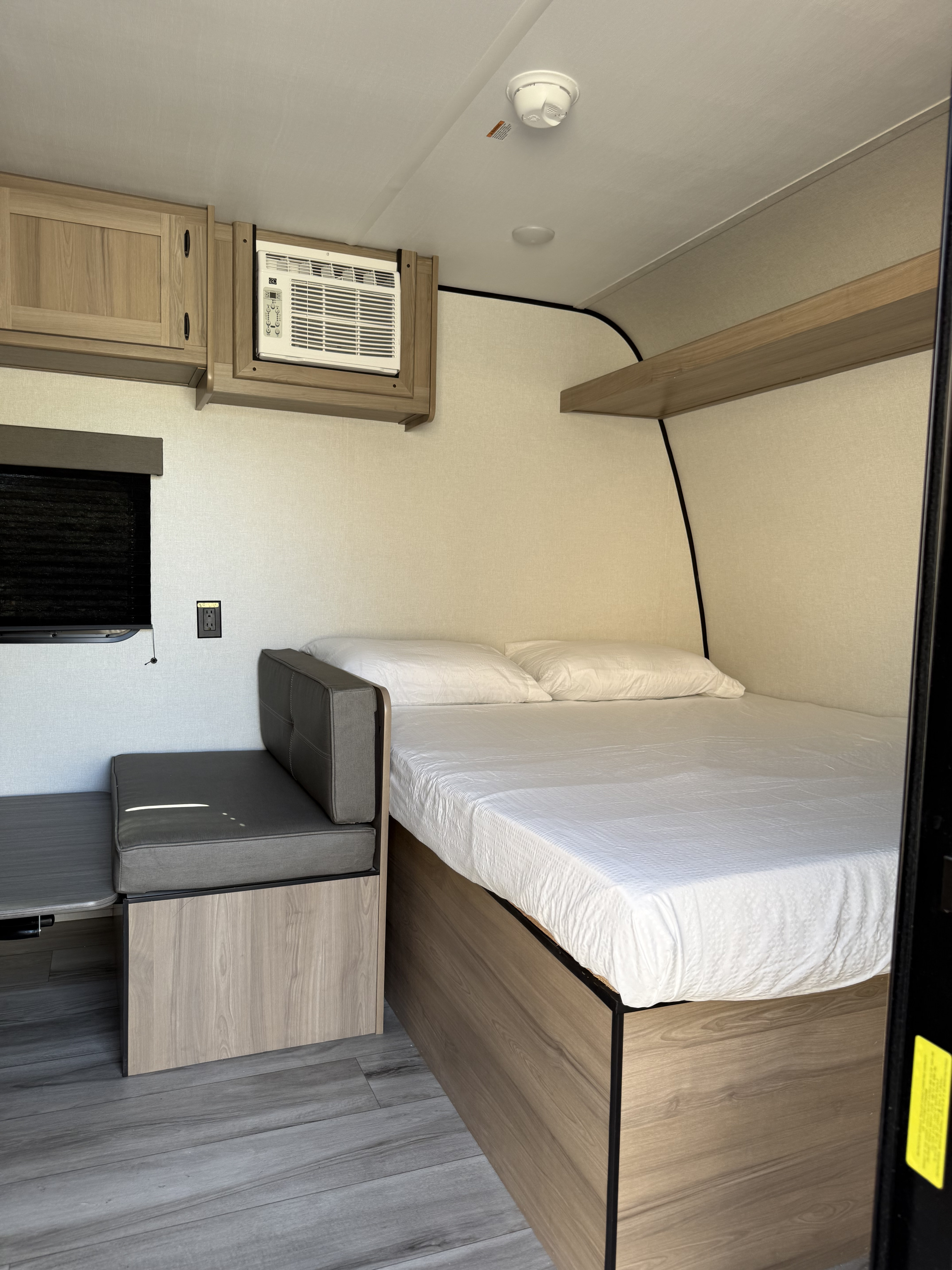 Cozy rv rental interior features a compact bed, gray bench, small table, AC unit, and overhead storage cabinets.. Coleman Keystone 2026