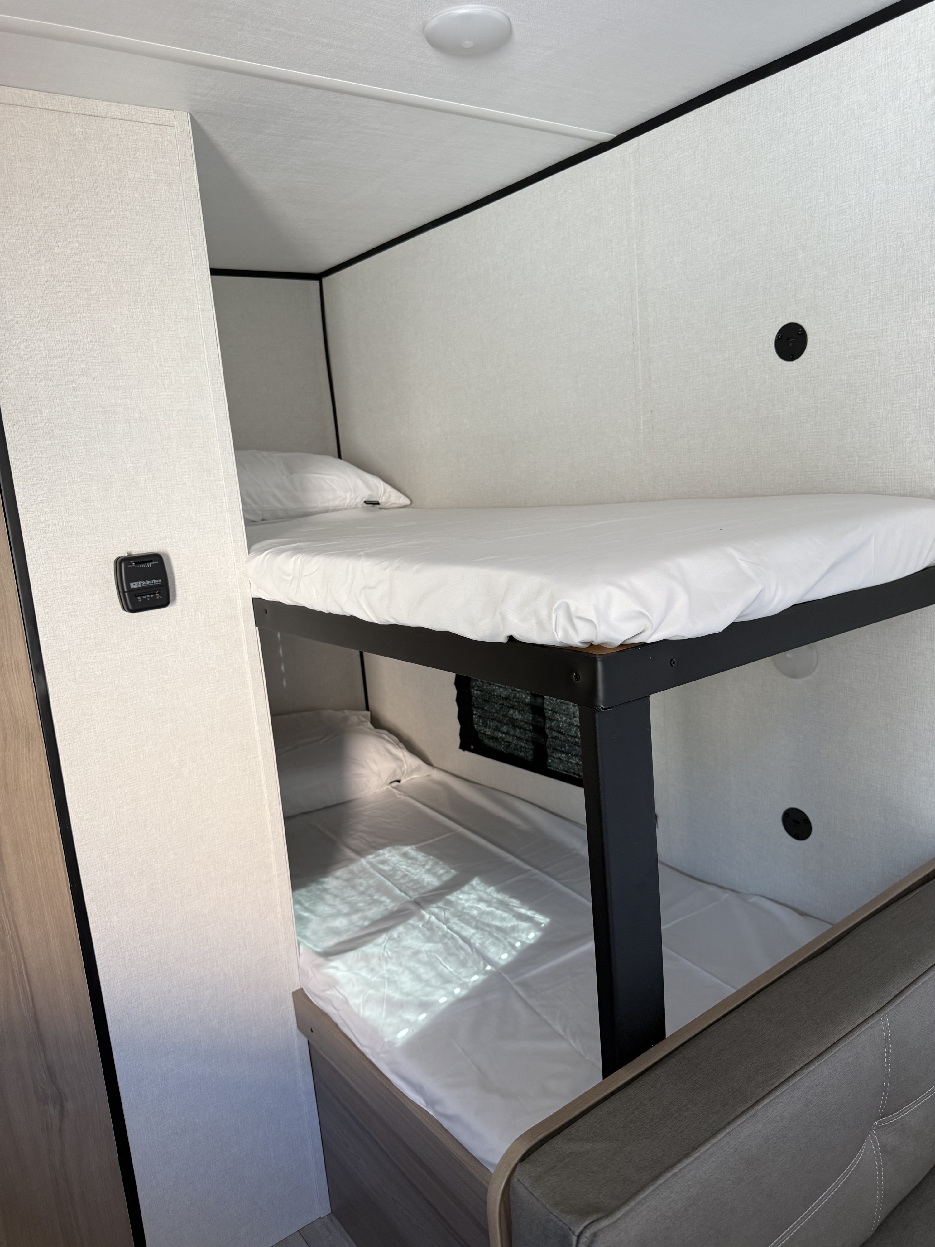 Cozy RV rental bunk beds with white sheets and pillows, offering compact sleeping in a travel trailer or camper.. Coleman Keystone 2026