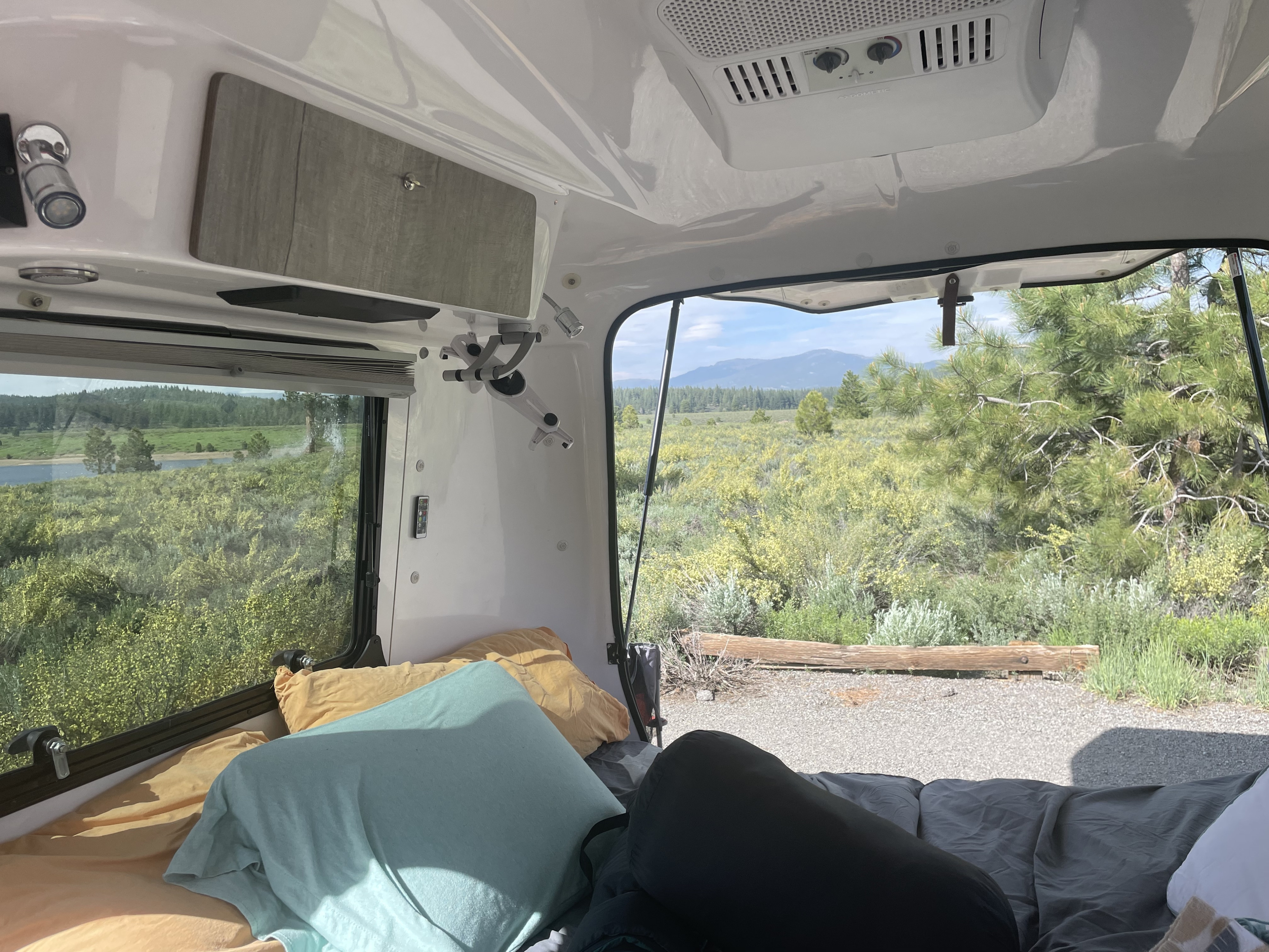 Inside a comfy rv rental, enjoy a scenic view of nature, mountains, and a lake from the bed.. Happier Camper HC1 2019