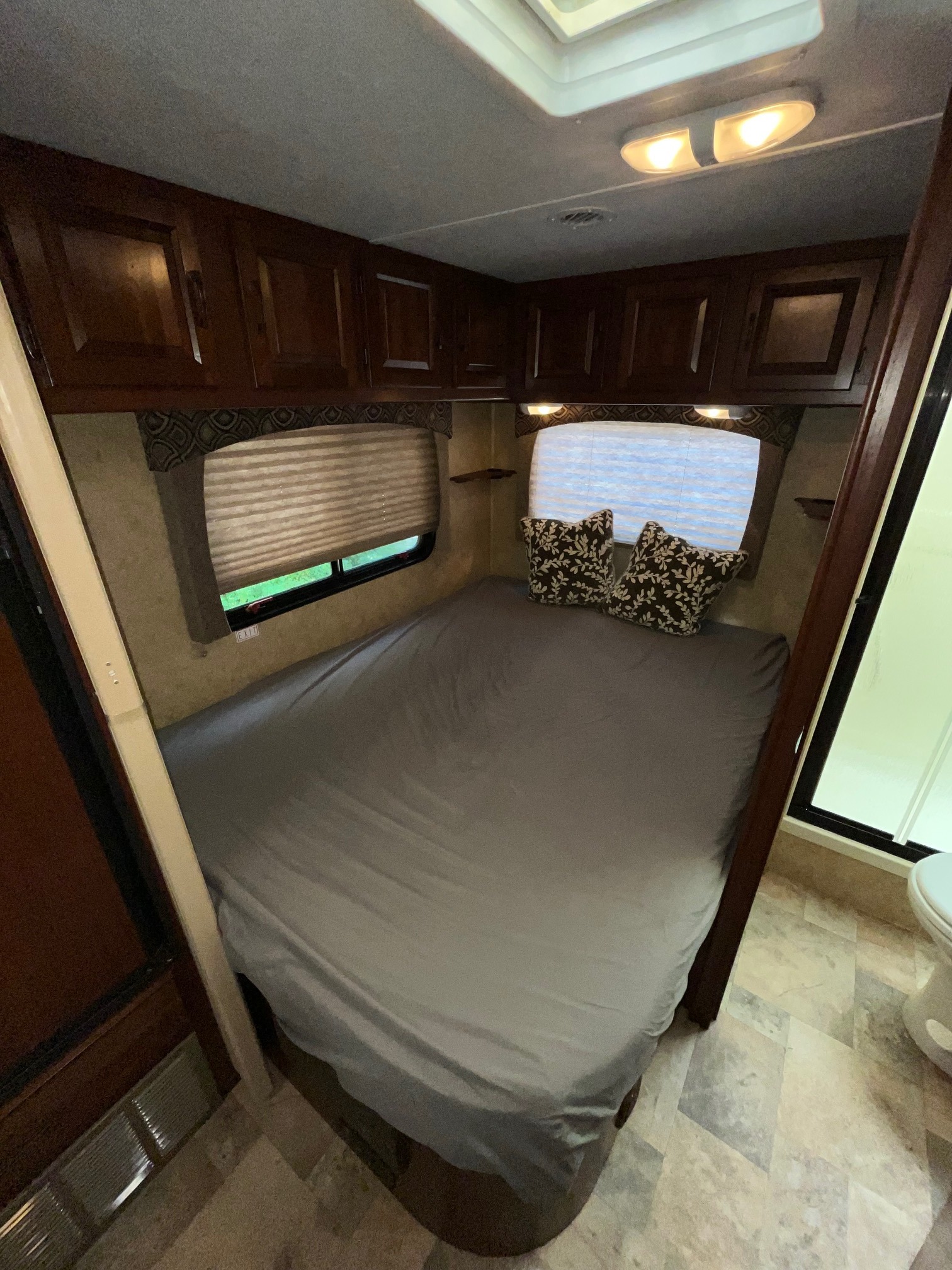 Cozy RV rental bedroom featuring a comfortable bed, overhead storage, and natural light from the window. Perfect for road trips!. Forest River Sunseeker 2014