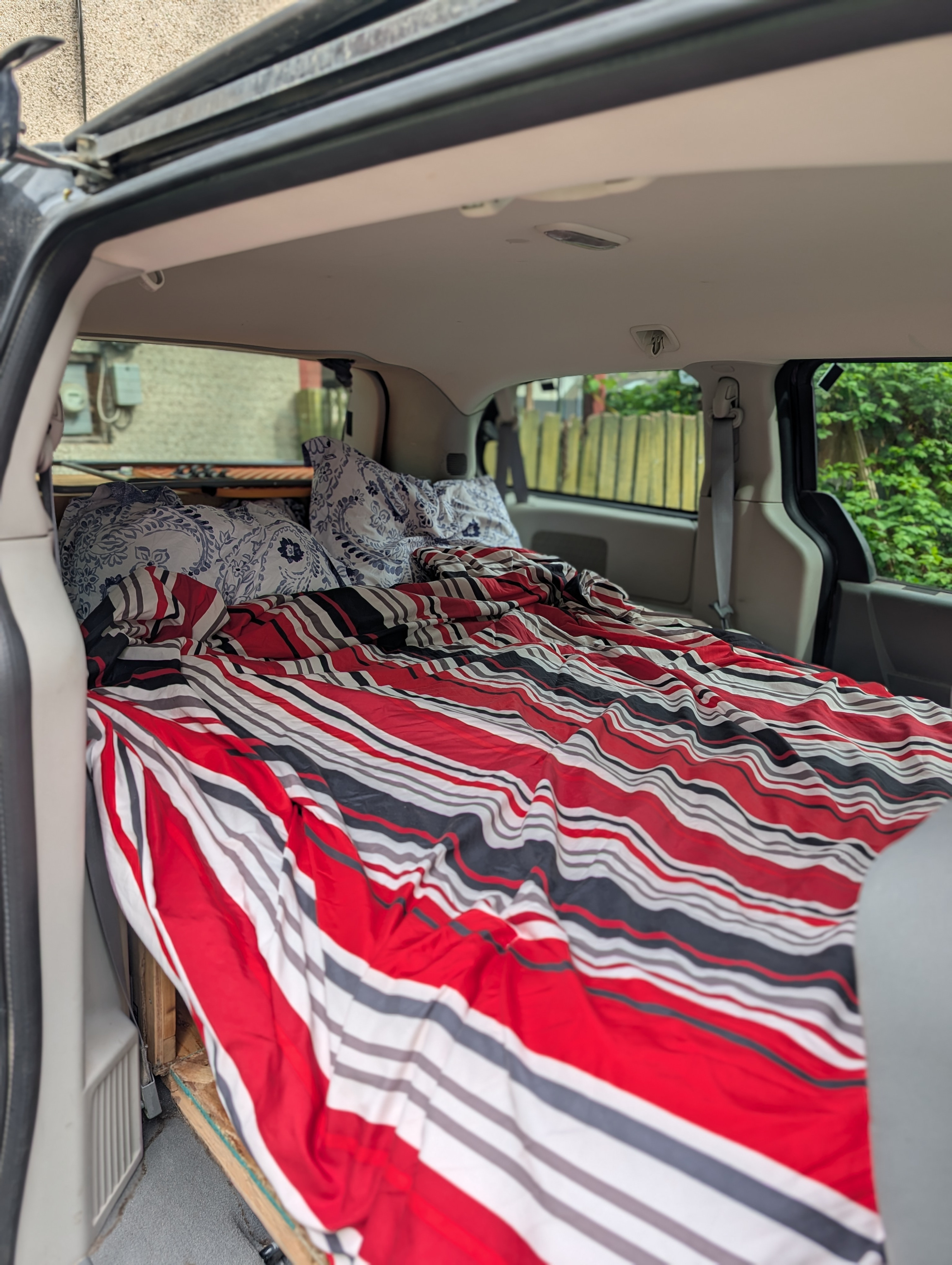 Cozy minivan conversion for your next RV rental road trip! Bed with striped comforter & pillows ready for car camping.. Dodge Grand Caravan 2009