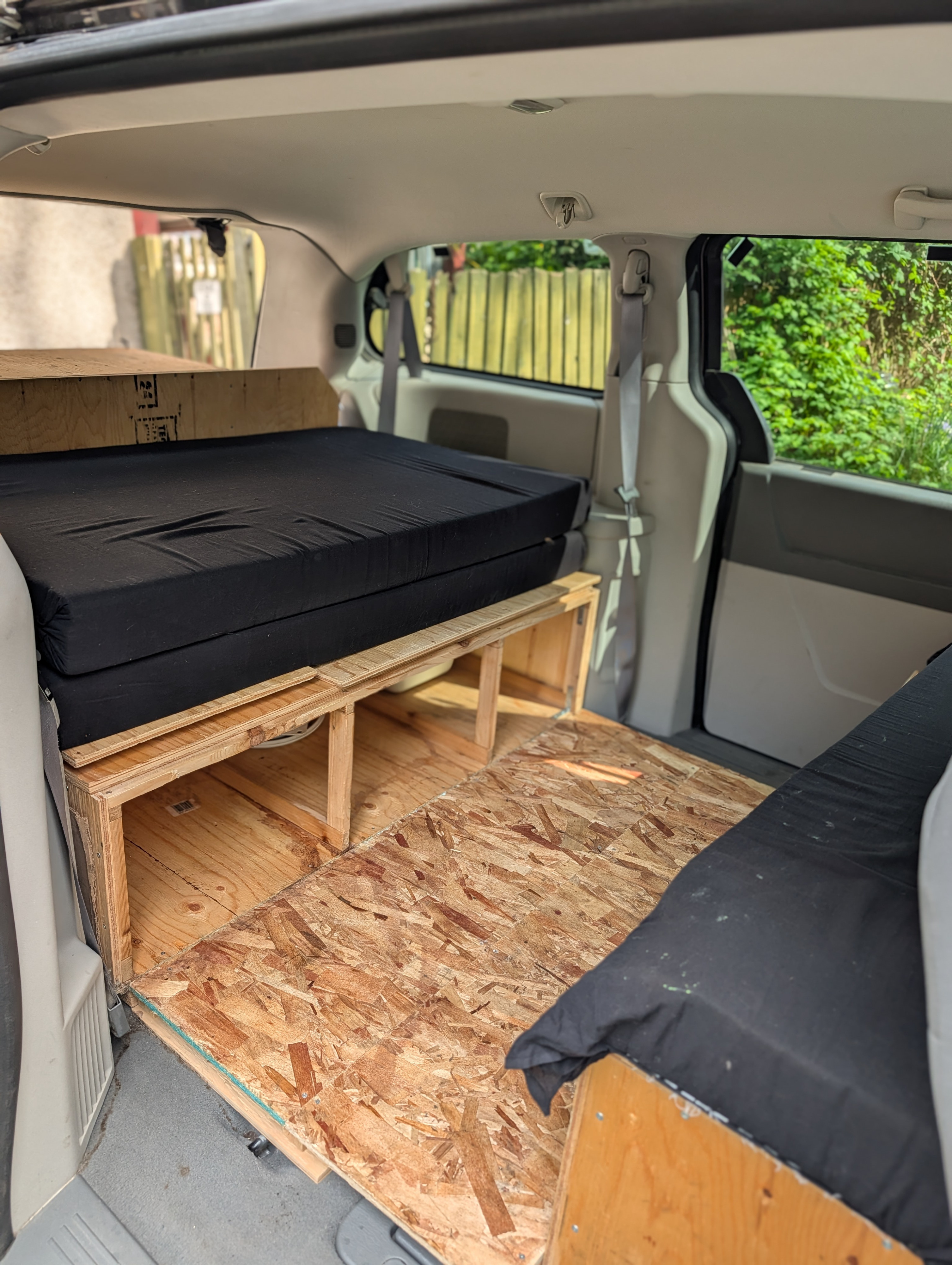 OSB floor, wooden platforms, and mattresses outfit this DIY van camper interior, ideal for an RV rental.. Dodge Grand Caravan 2009