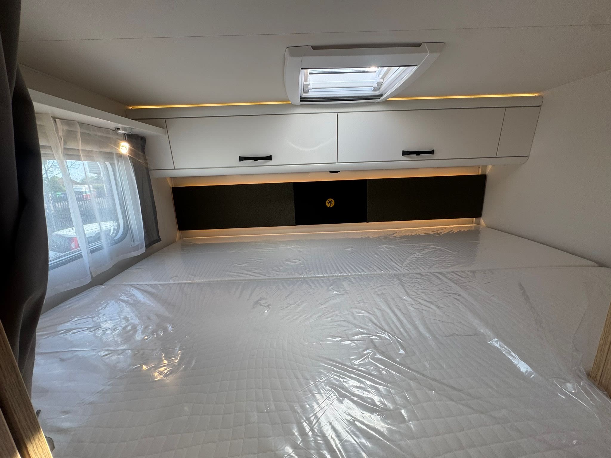 Spacious rv rental bedroom with a new, plastic-covered bed, overhead storage, skylight, and ambient light.. Sunlight A70 2026