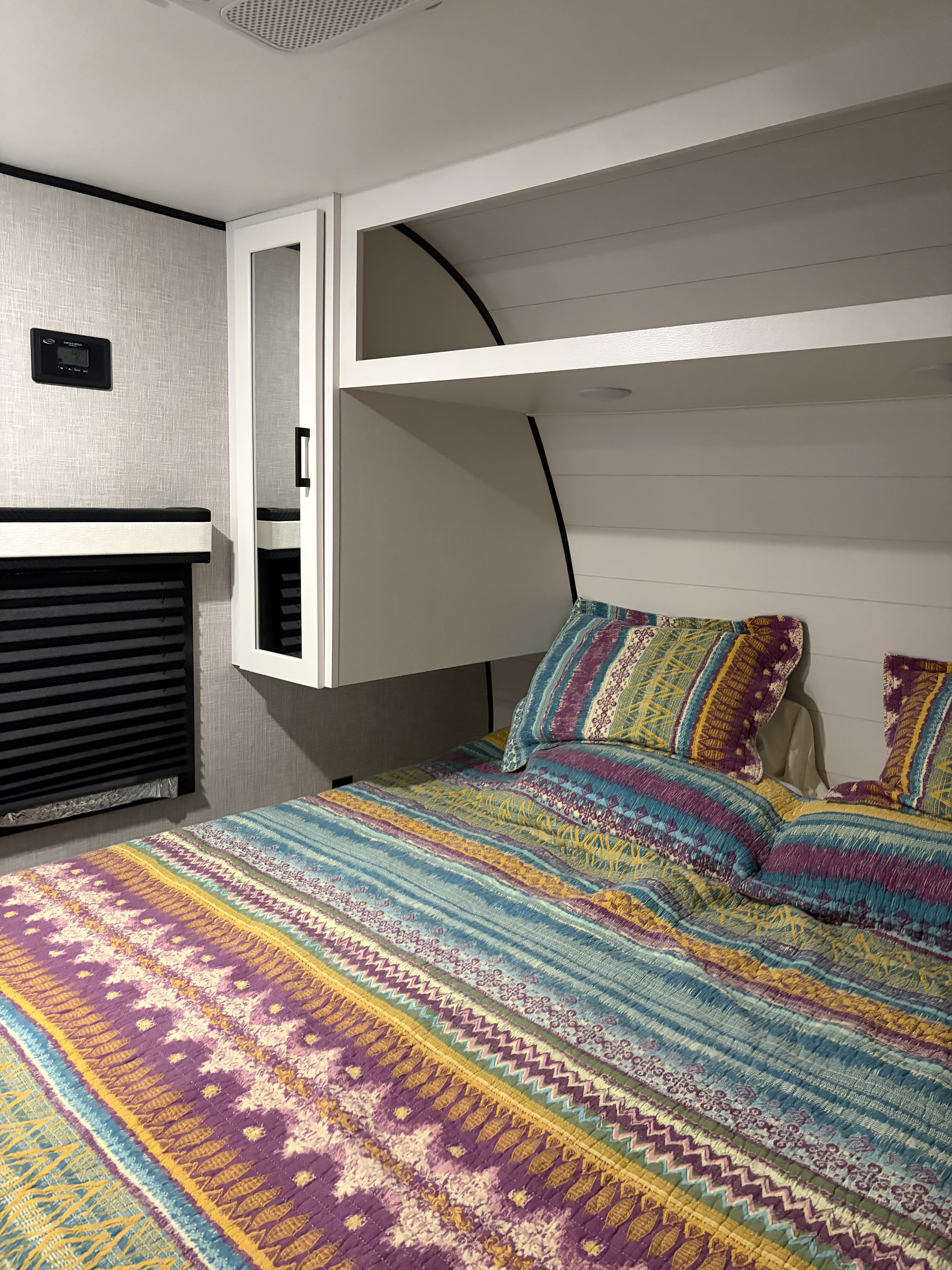 Relaxing rv rental bedroom featuring a vibrant bed, overhead storage, and a climate control panel for comfort.. Jayco Jay Flight SLX 2025
