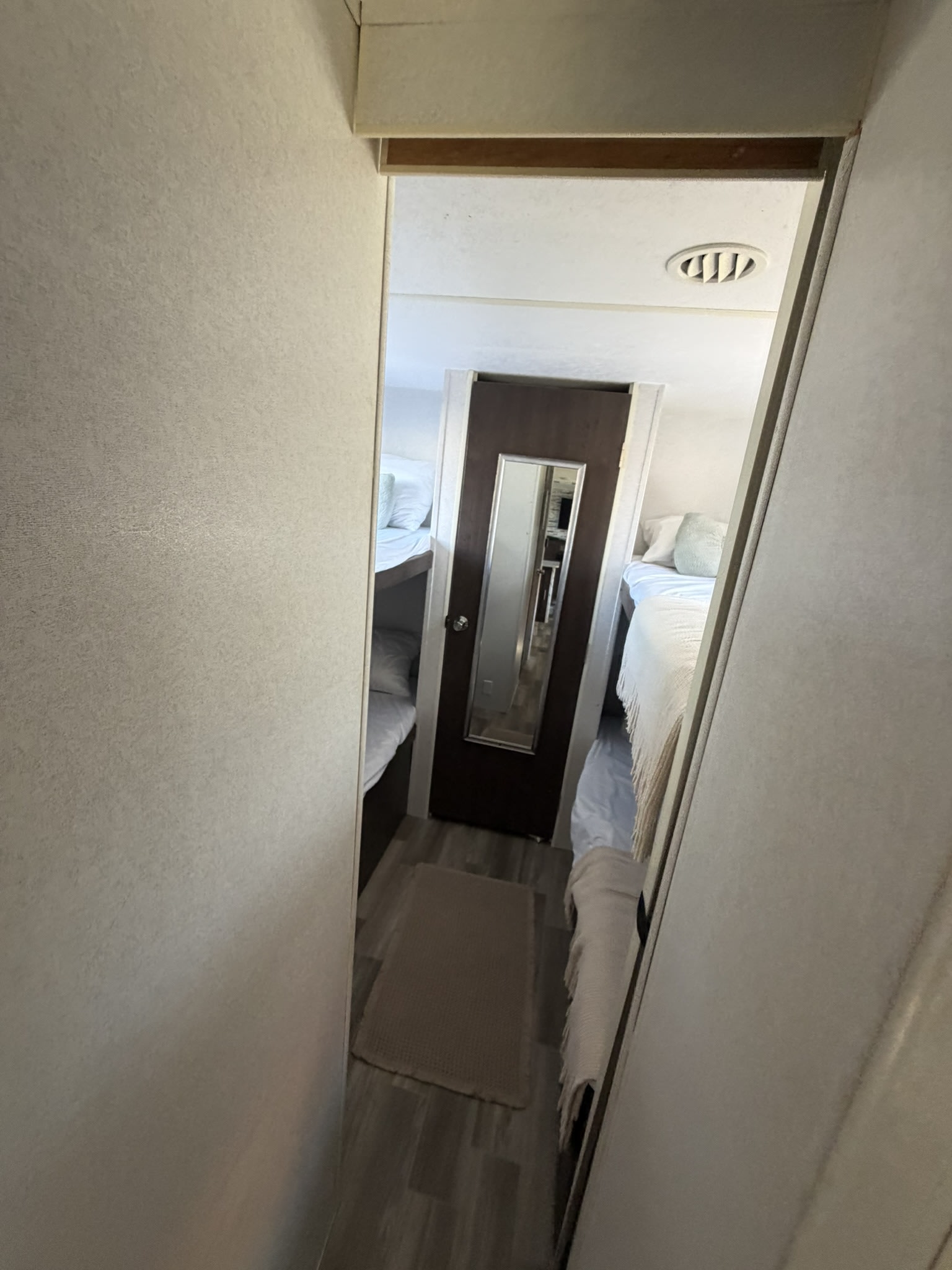 Compact RV rental interior: A narrow hallway with bunk beds on both sides leads to a door with a mirror at the far end.. Forest River Wildwood 2020