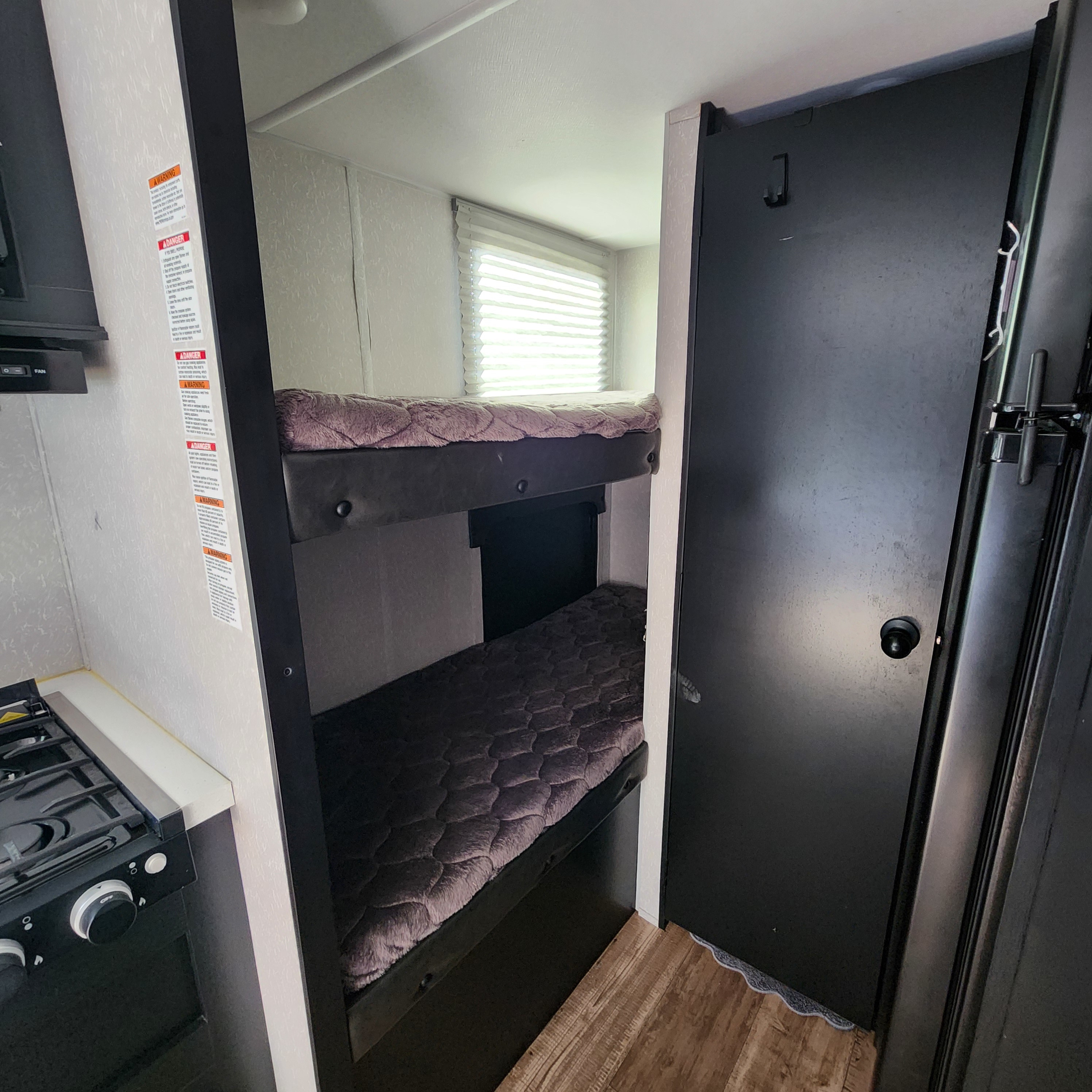 RV rental: bunk beds with patterned mattresses, a kitchen stove, and a dark door for travel or camping adventures.. Forest River Cherokee Wolf Pup Black Label 2022
