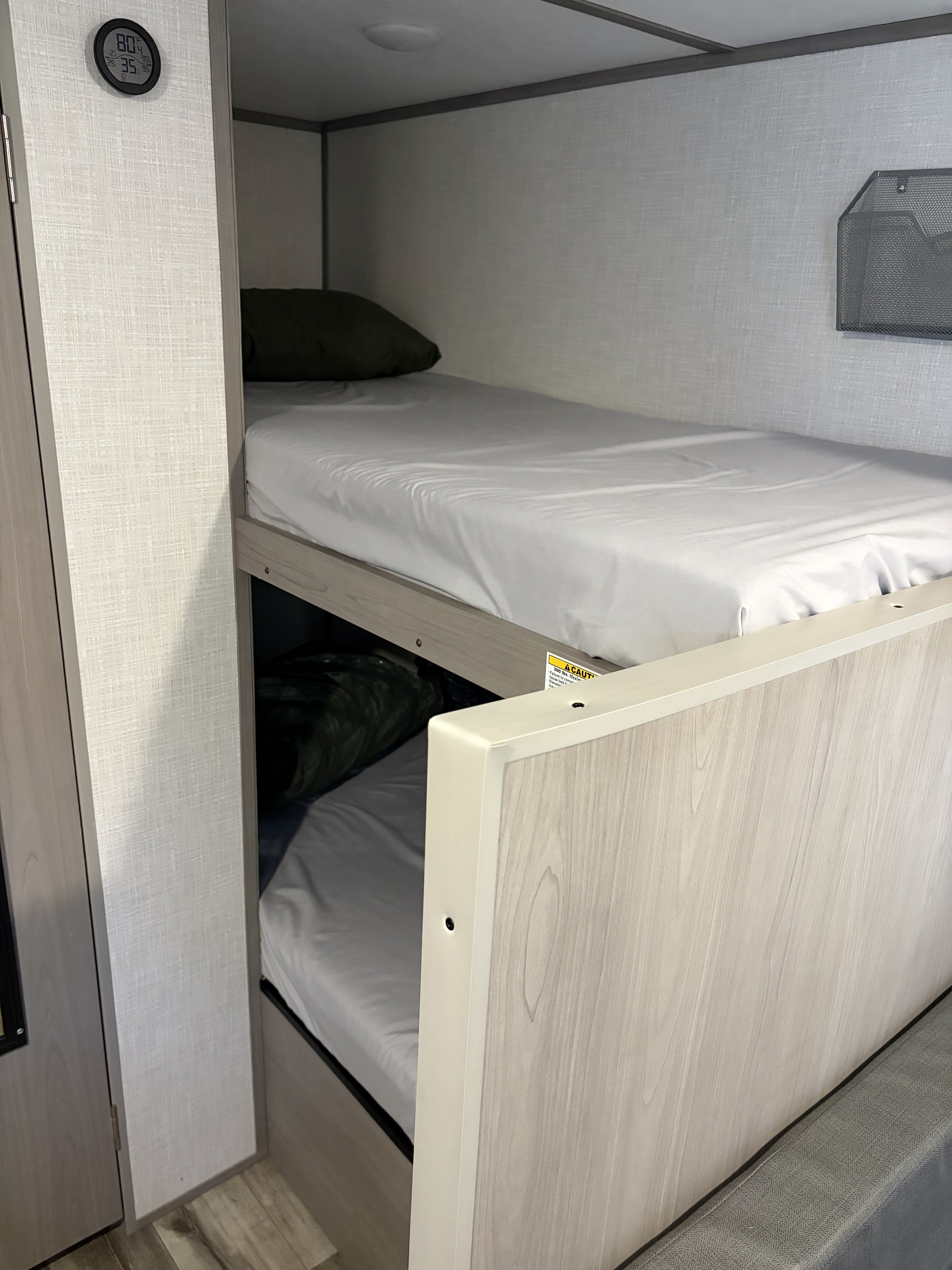 RV rental bunk beds feature light wood, white bedding, a digital thermometer (80°F), and mesh wall storage.. Dutchmen Coleman Lantern LT 2022