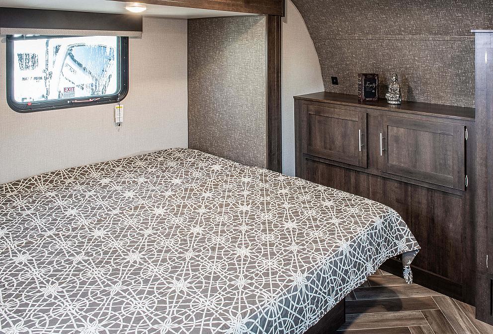 This RV rental offers a cozy bedroom with a patterned bed, window (EXIT visible), and built-in storage.. Sportsmen LE 2020