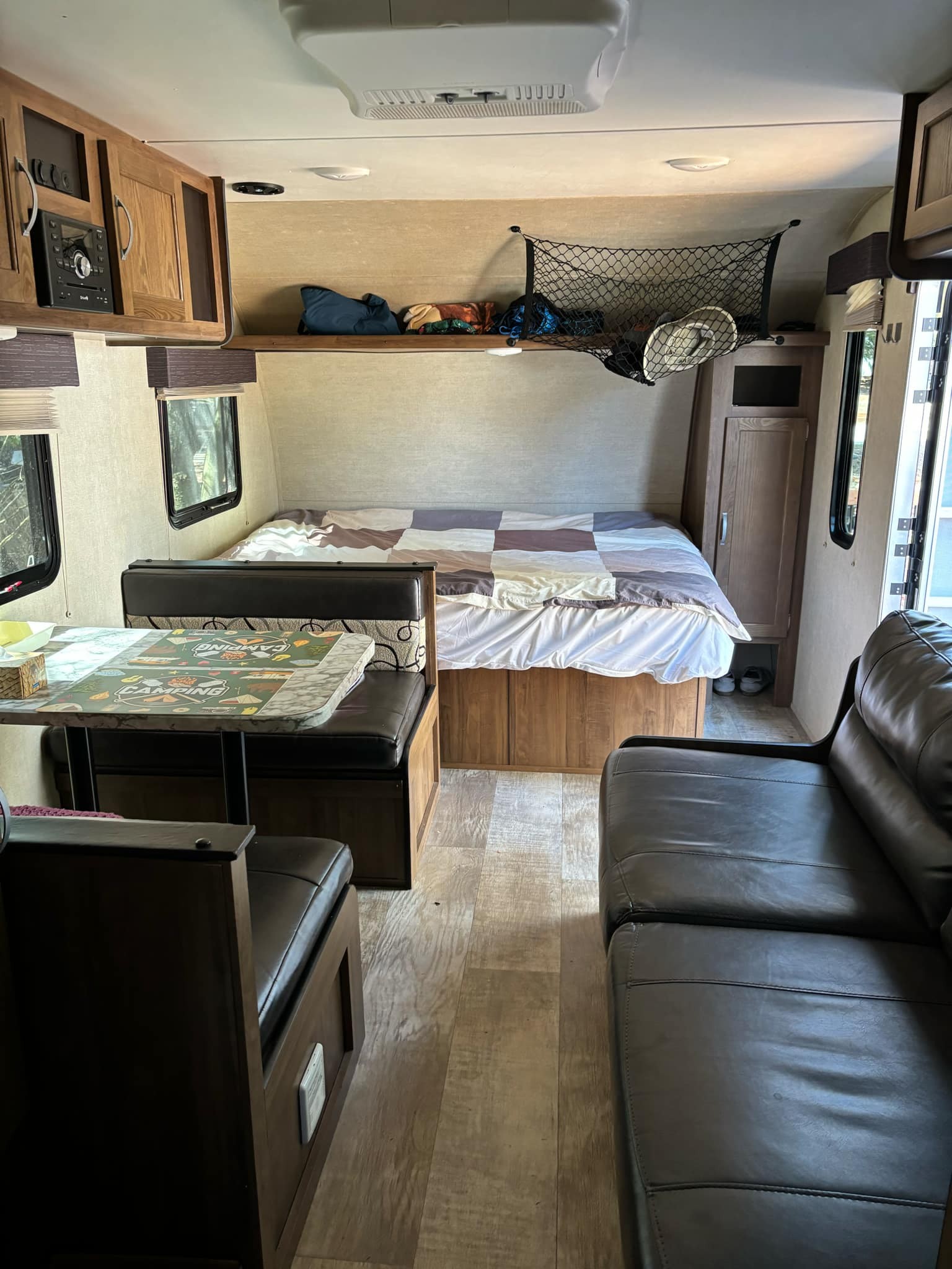 An RV rental interior features a cozy bed, dinette, dark leather sofa, and overhead storage.. Gulf Stream Ameri-Lite 2019