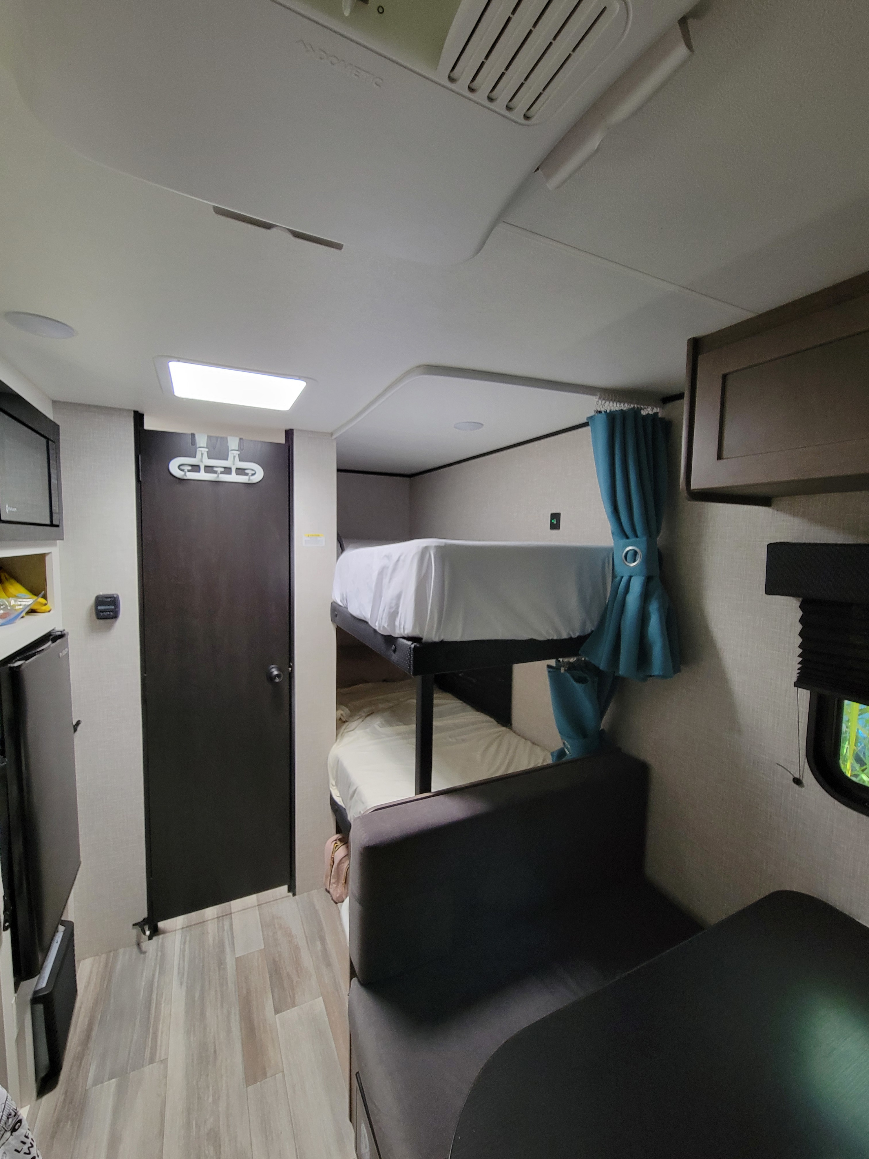 RV rental interior with cozy bunk beds, a compact kitchen (fridge, microwave), and a dinette, featuring light flooring.. Jayco Jay Flight SLX 2025
