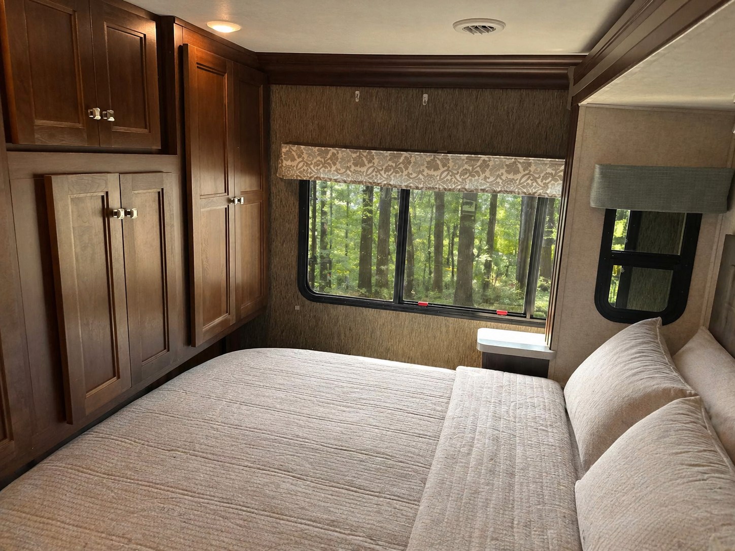 RV rental bedroom with a comfy bed, wooden cabinets, and a serene forest view from a large window, perfect for nature lovers.. Forester Forester Motorhome 2018