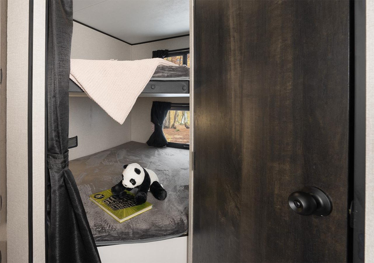 Cozy bunk beds in this RV rental. A plush panda and a book rest on the lower bunk, with a forest view outside the window.. Starcraft Autumn Ridge 2018