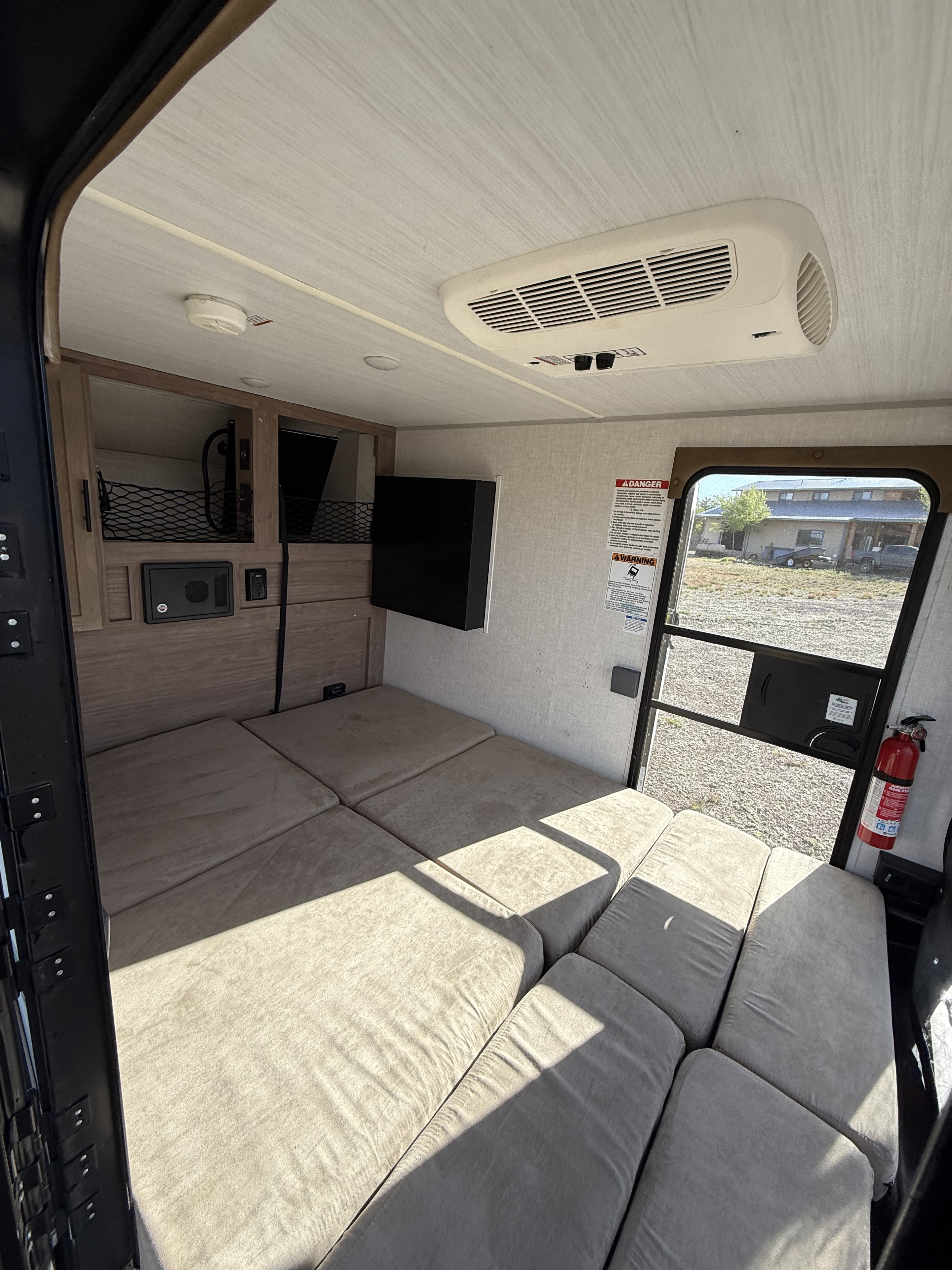 Inside an rv rental: versatile cushioned seating converts to a bed, with AC, TV, and fire extinguisher near the door.. Forest river No boundaries 10.6 2019