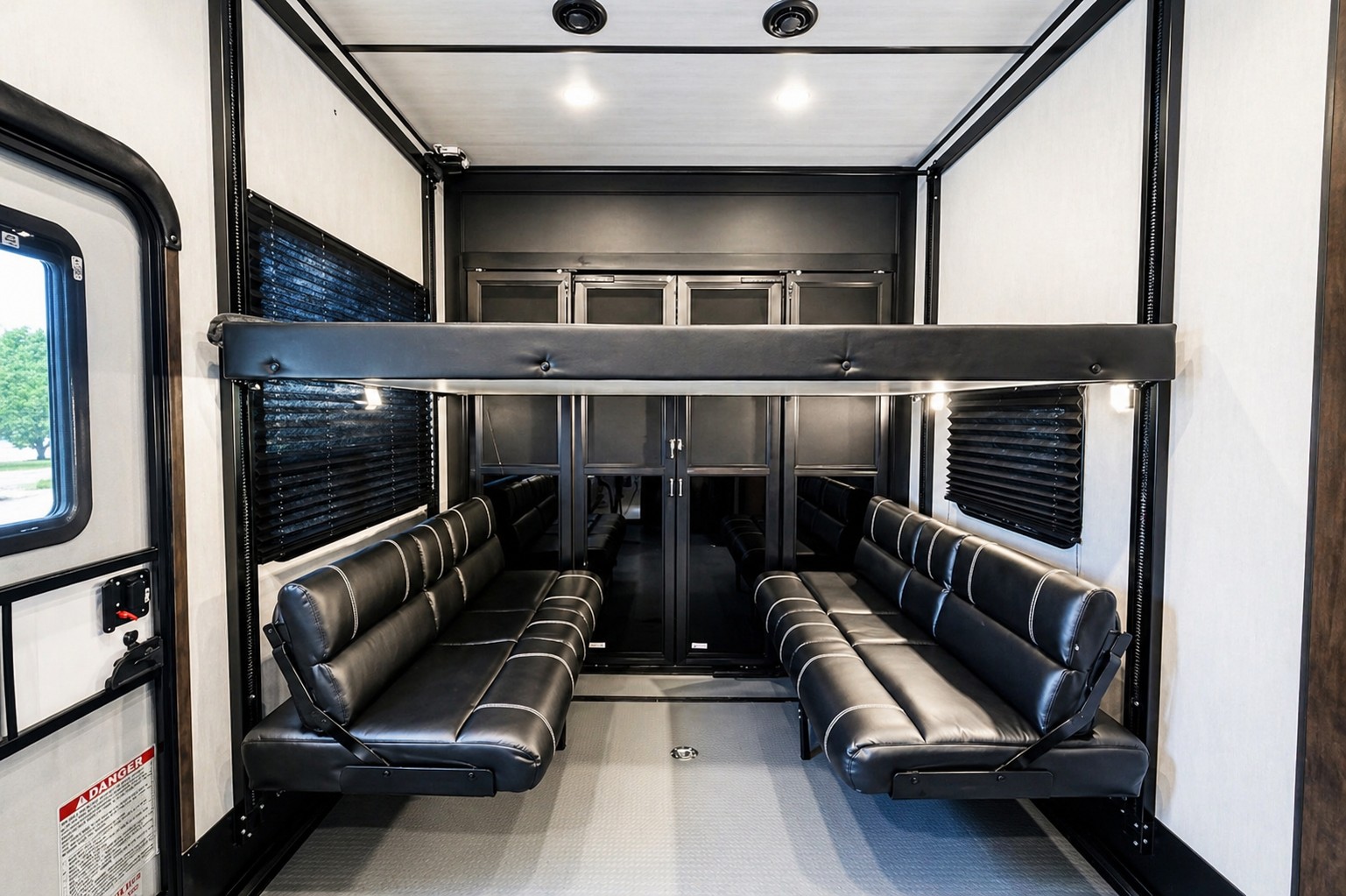 Inside an RV rental toy hauler: garage space with two black convertible sofas and an overhead bunk bed.. Dutchmen Triton 4271 2022