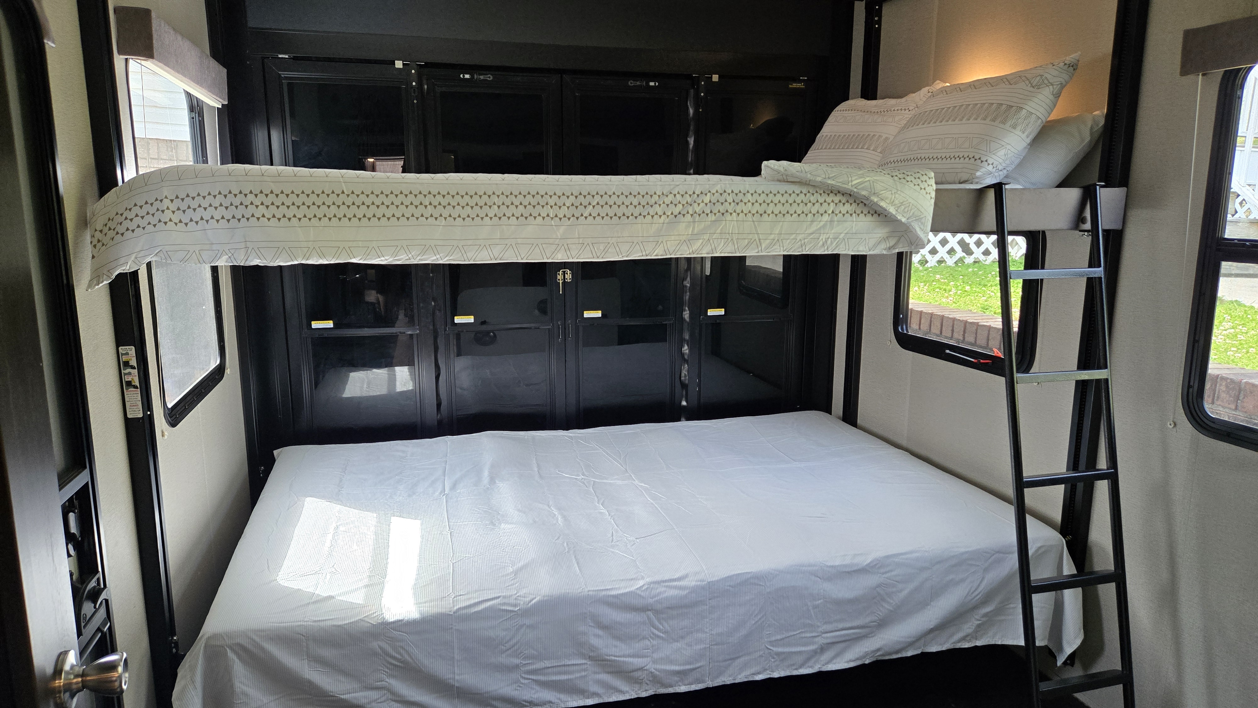 RV rental: a cozy sleeping area featuring lower and upper bunk beds with patterned bedding and a ladder. Windows show greenery.. Grand Design Momentum 2020