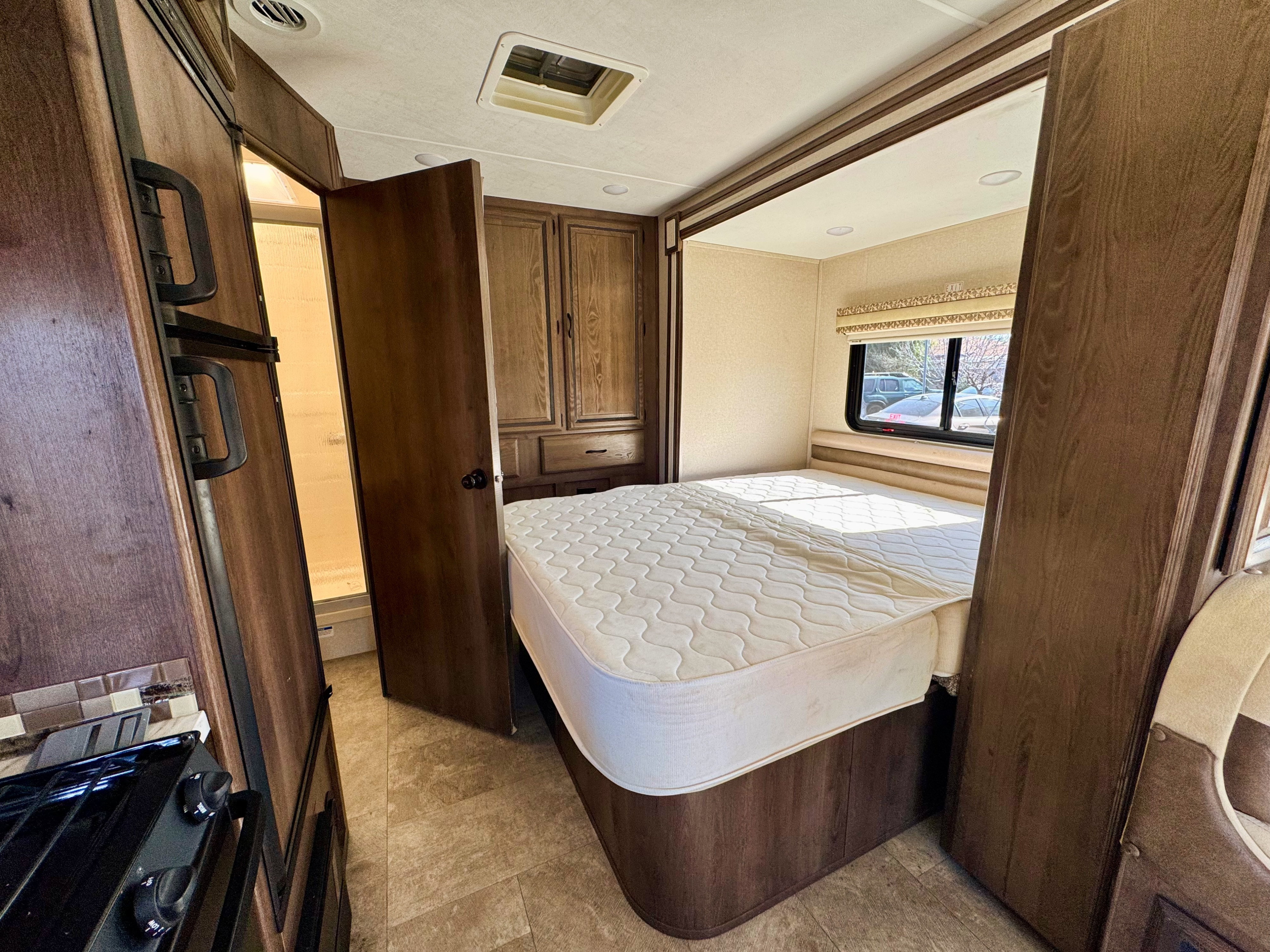 This rv rental interior showcases a cozy bedroom, a small kitchen with a stove, and a visible bathroom, all in a compact camper design.. Coachmen Prism 2019