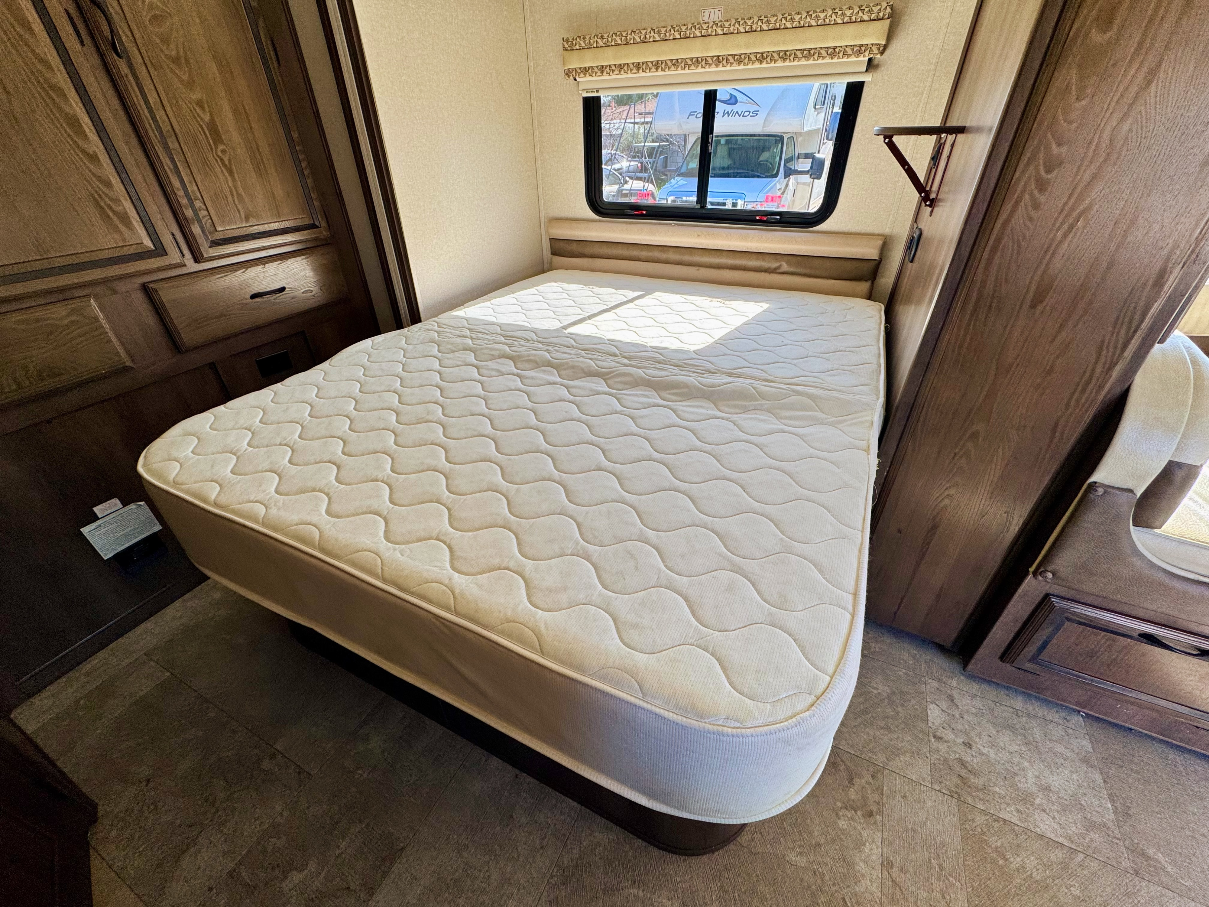 RV rental bedroom features a comfortable mattress, overhead wooden cabinets, and a window view from an RV.. Coachmen Prism 2019