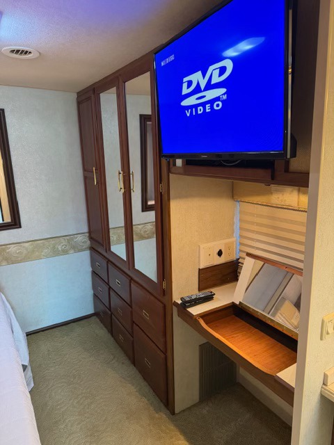 Inside an rv rental bedroom: a large wooden wardrobe, TV showing "DVD VIDEO", and a vanity with mirror.. Winnebago Adventurer 2004