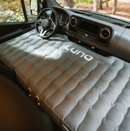 A LUNA inflatable mattress fills the front of this RV rental van for camping, transforming the driver and passenger area into a comfy bed.. Winnebago Revel 2025
