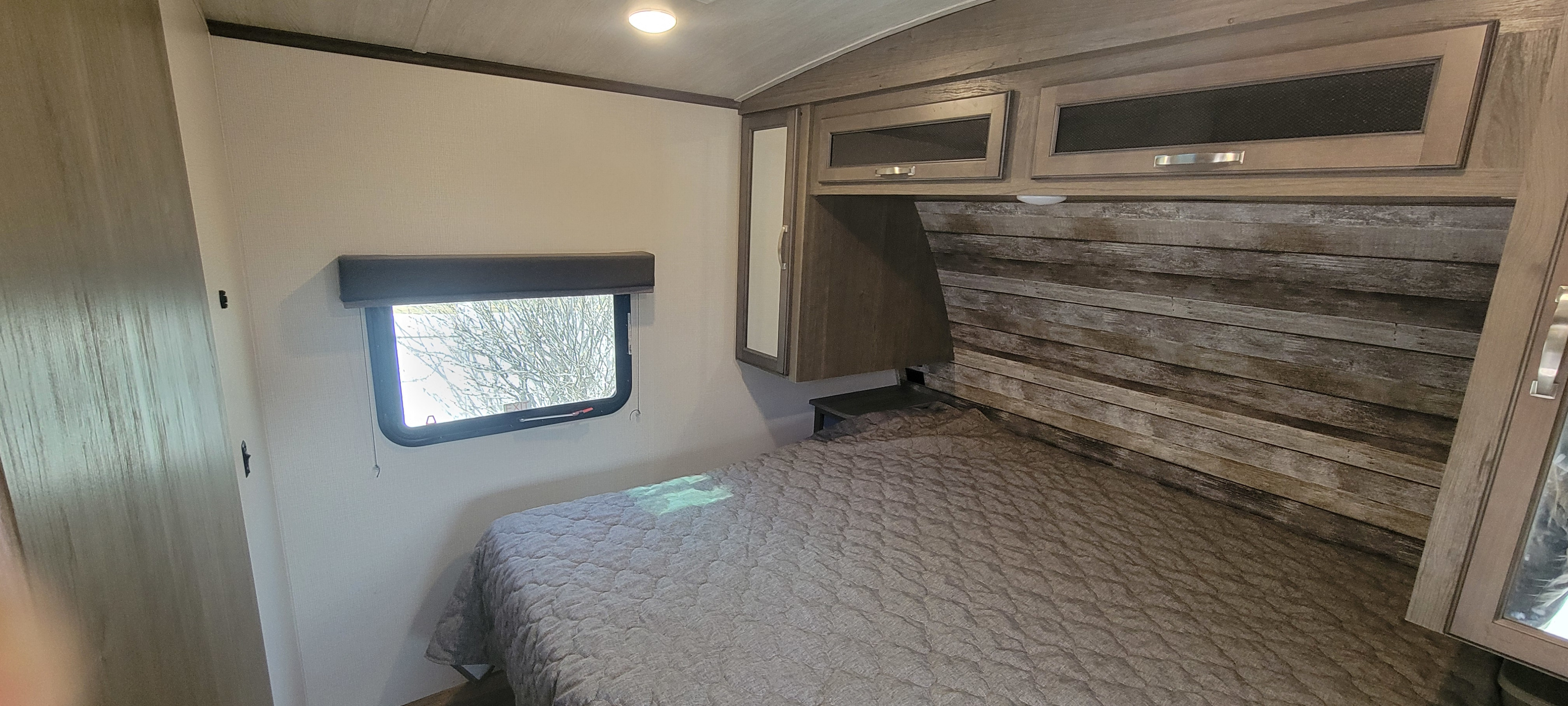 Comfortable RV rental bedroom with quilted bed, window, overhead cabinets, and a distressed wood-plank headboard.. Keystone RV Cougar 2021