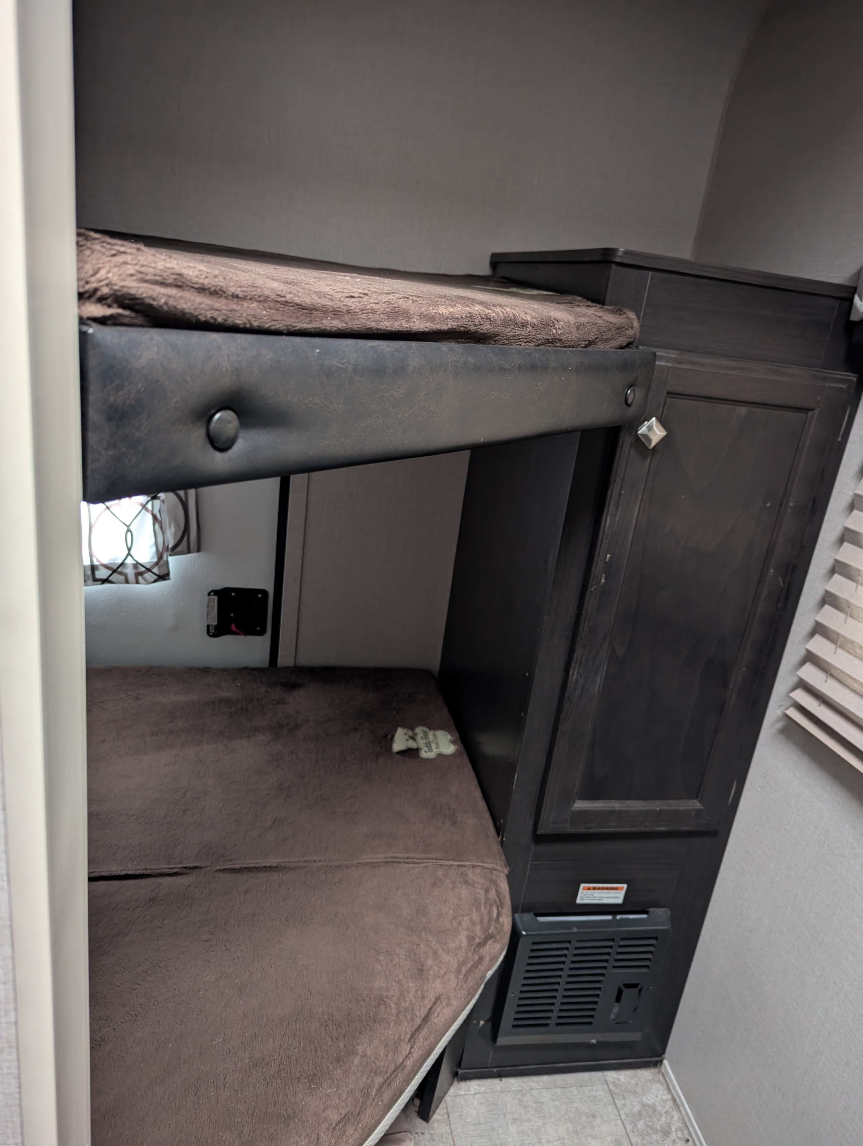 Cozy bunk beds in an RV rental, featuring soft brown blankets, dark wood cabinets, and a lower heater vent.. Sonic Lite 2019
