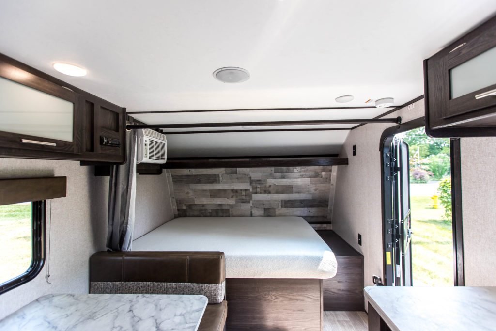 Modern RV rental interior with a bed, dinette, and AC unit. An open door provides a view to the outside.. Dutchmen Coleman Lantern LT 2021