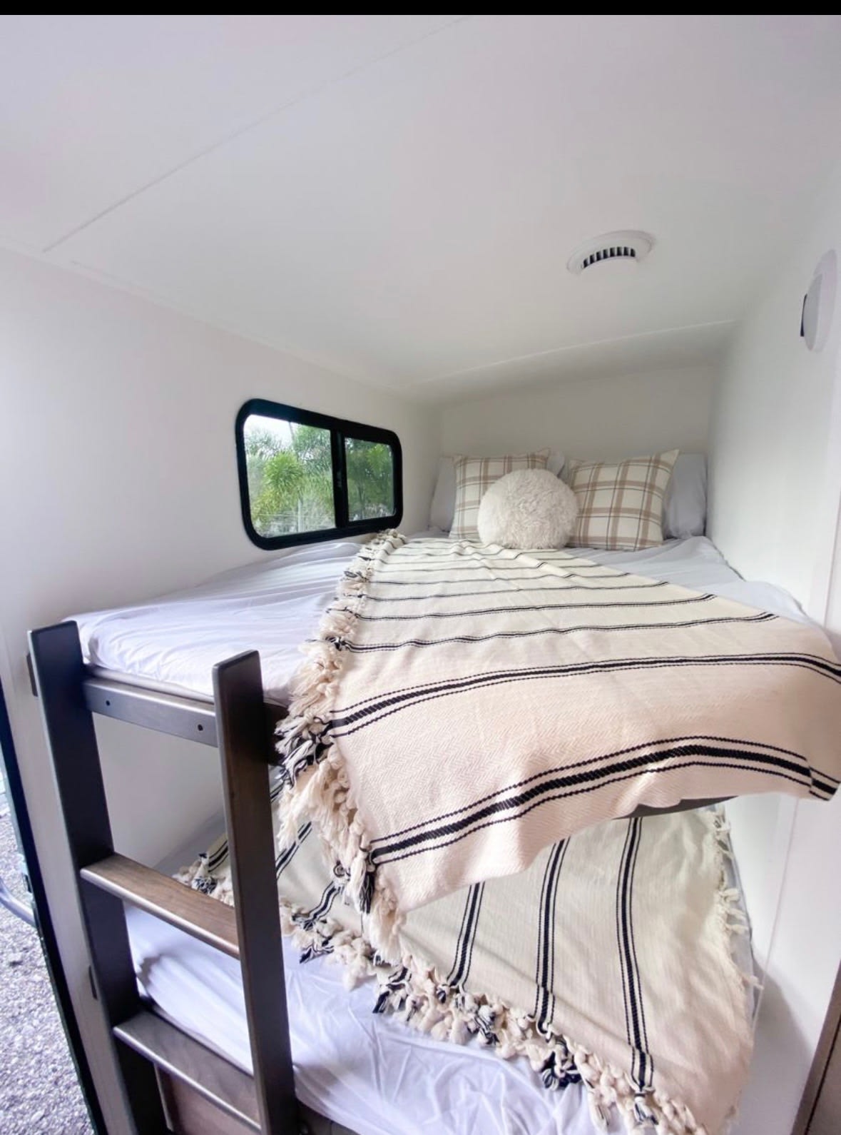 Comfortable bunk beds in a clean, bright RV rental. Features cozy striped blankets, plaid pillows, and a window view.. Grand Design Imagine 2020