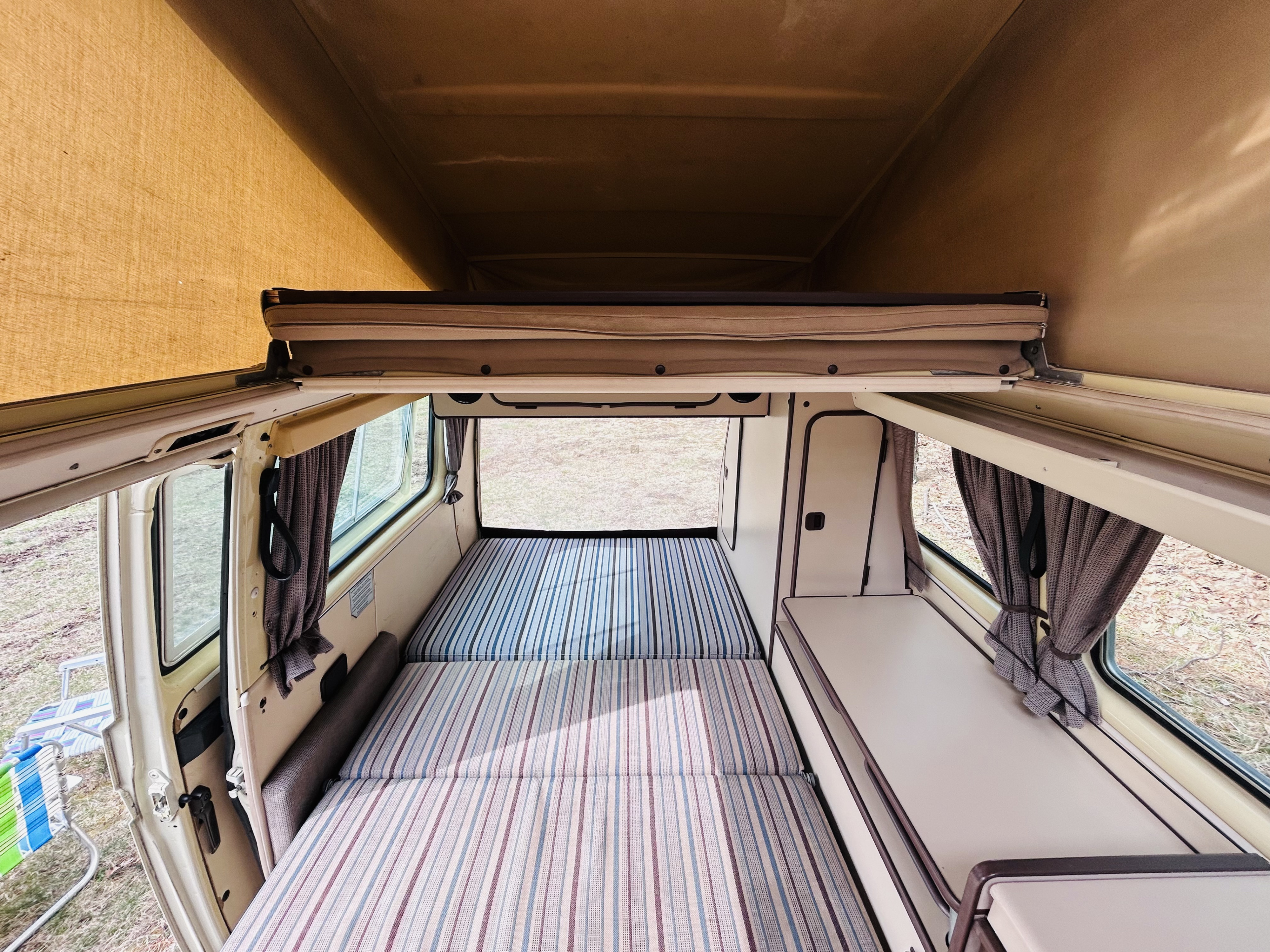 Cozy pop-top camper van interior featuring striped beds, cabinets, and open windows; perfect for your next rv rental.. Volkswagen T3 Westfalia 1984