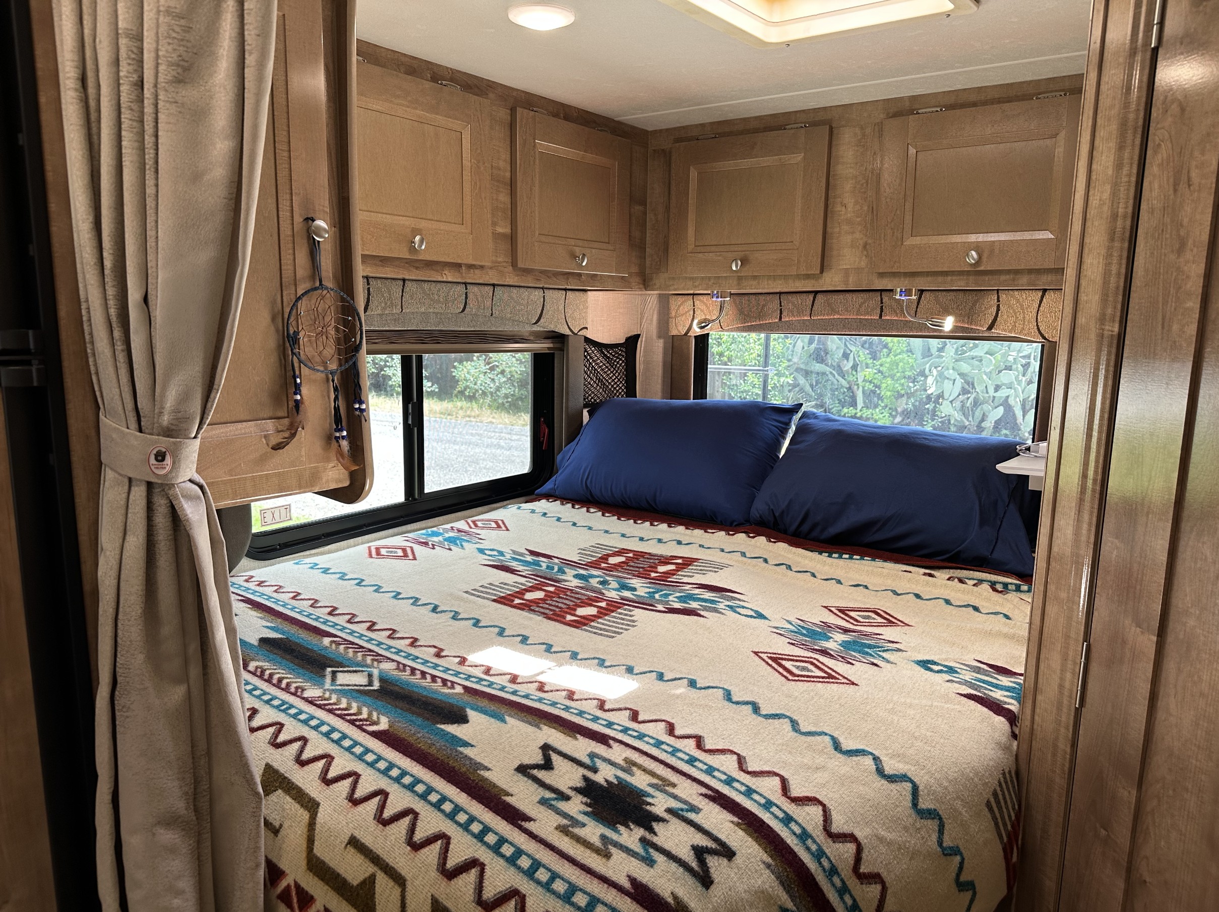 Cozy RV rental bedroom with patterned blanket, blue pillows, and scenic windows. Ideal for your next road trip adventure!. FORD COACHMAN LEPRECHAUN 2020