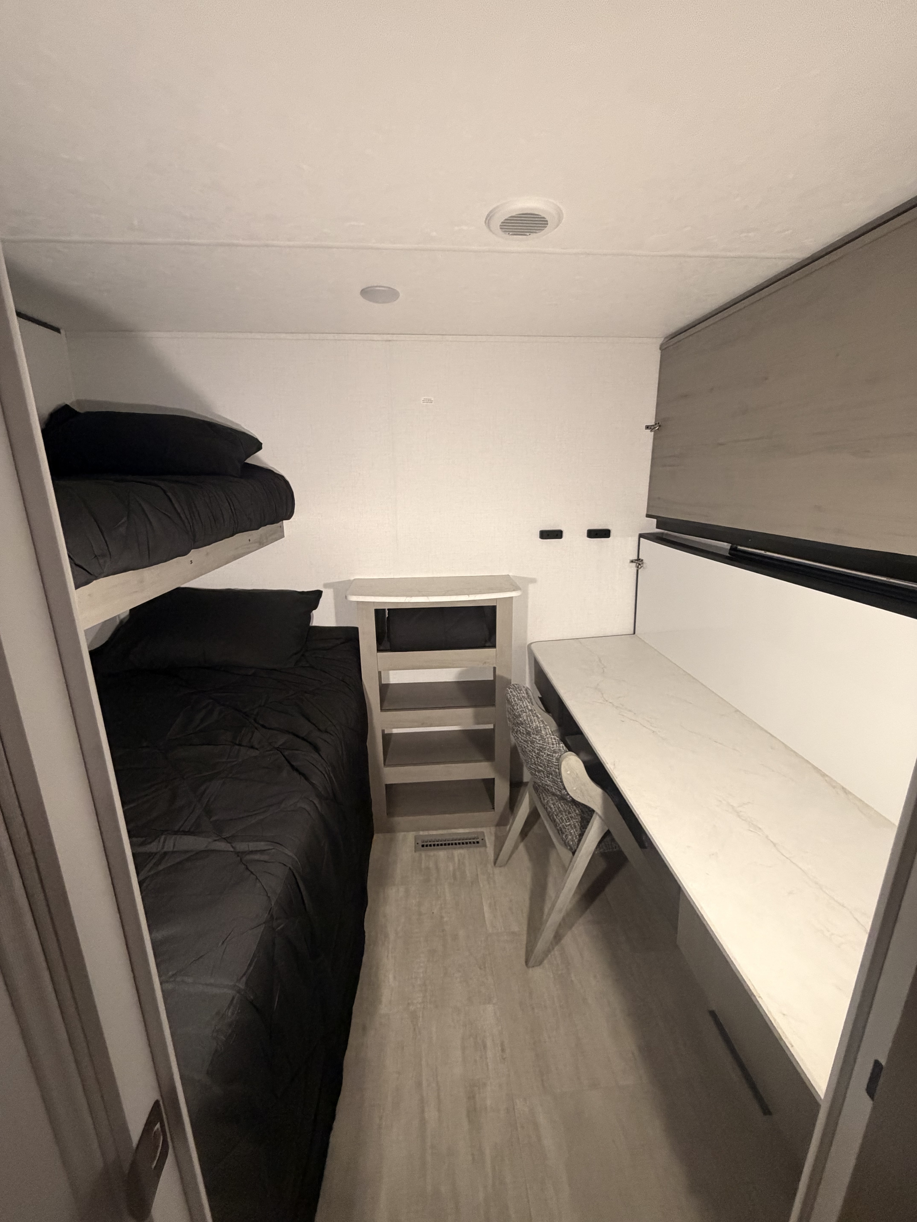 Compact RV rental room featuring bunk beds, a desk, and shelving for functional use.. Dutchmen Colorado 2025