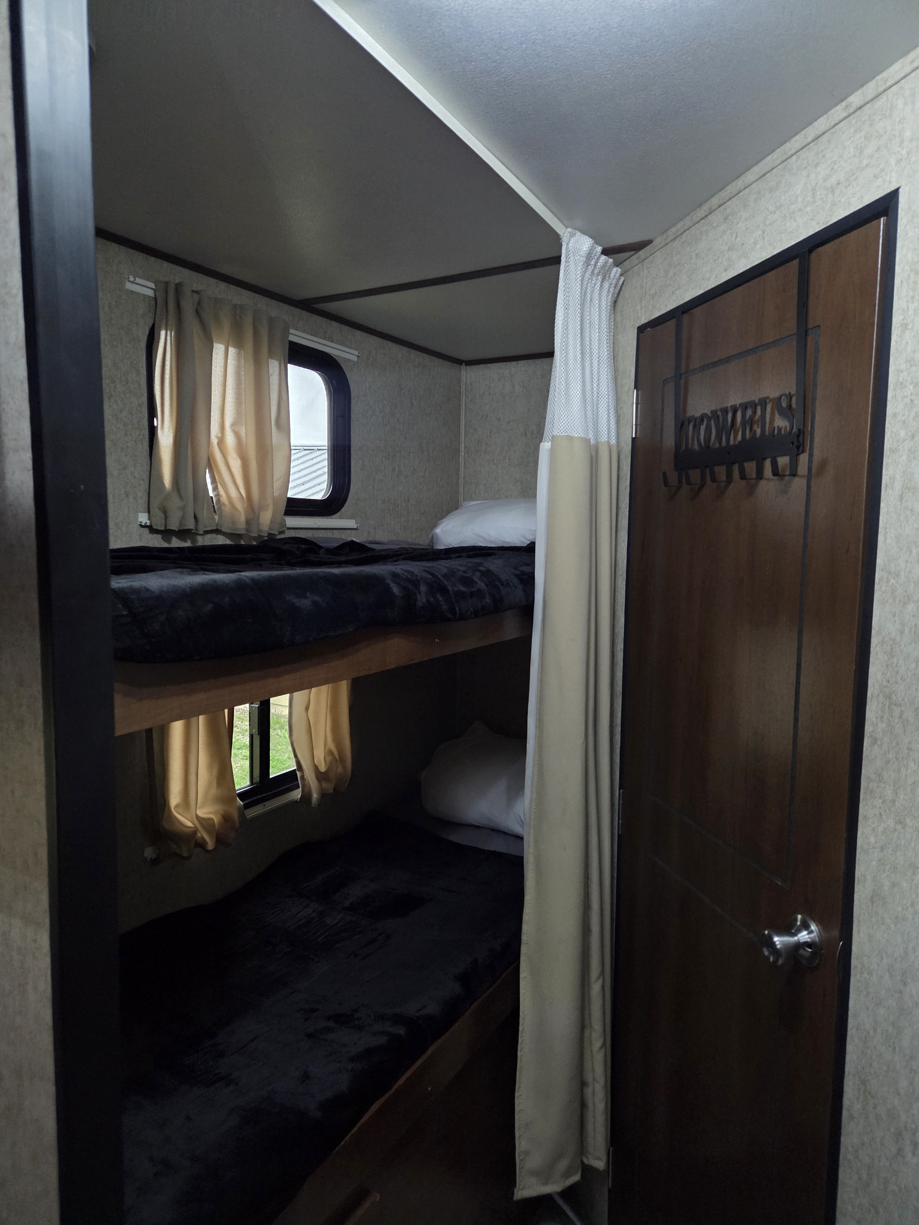 Cozy RV rental bunk beds with windows and a door featuring a "TOWELS" hanger, ready for a comfortable stay.. Nomad Nomad Trailer 2016