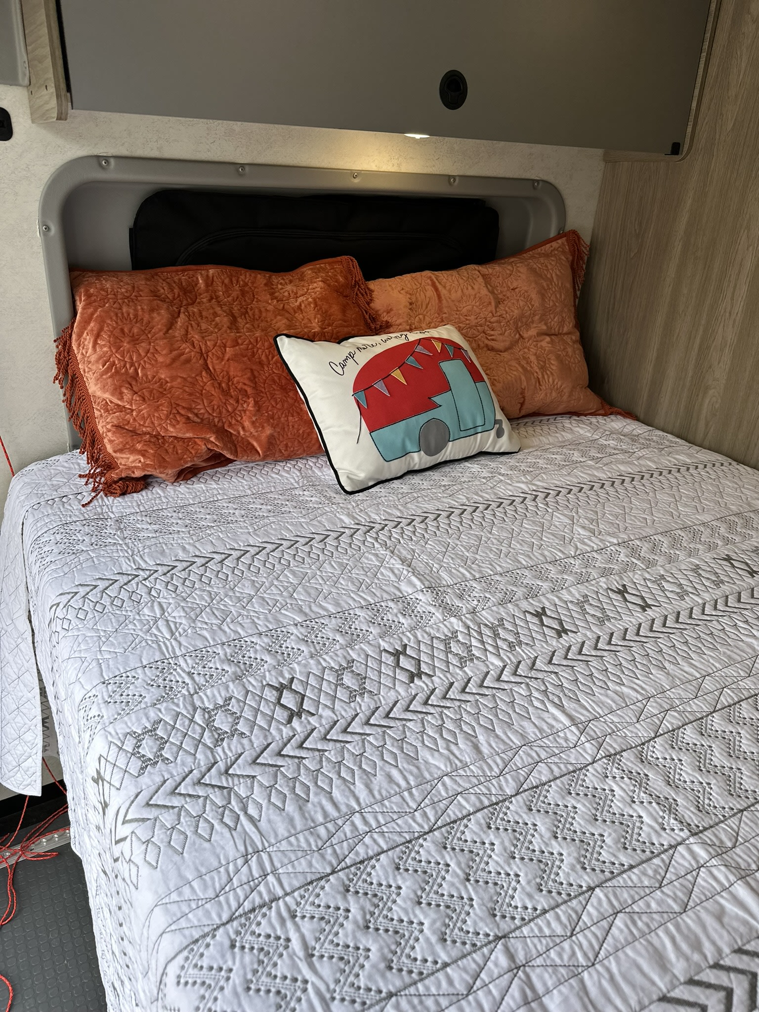 Cozy RV rental bed with a white geometric quilt, plush orange pillows, and a decorative camper cushion.. Winnebago Solis 2022