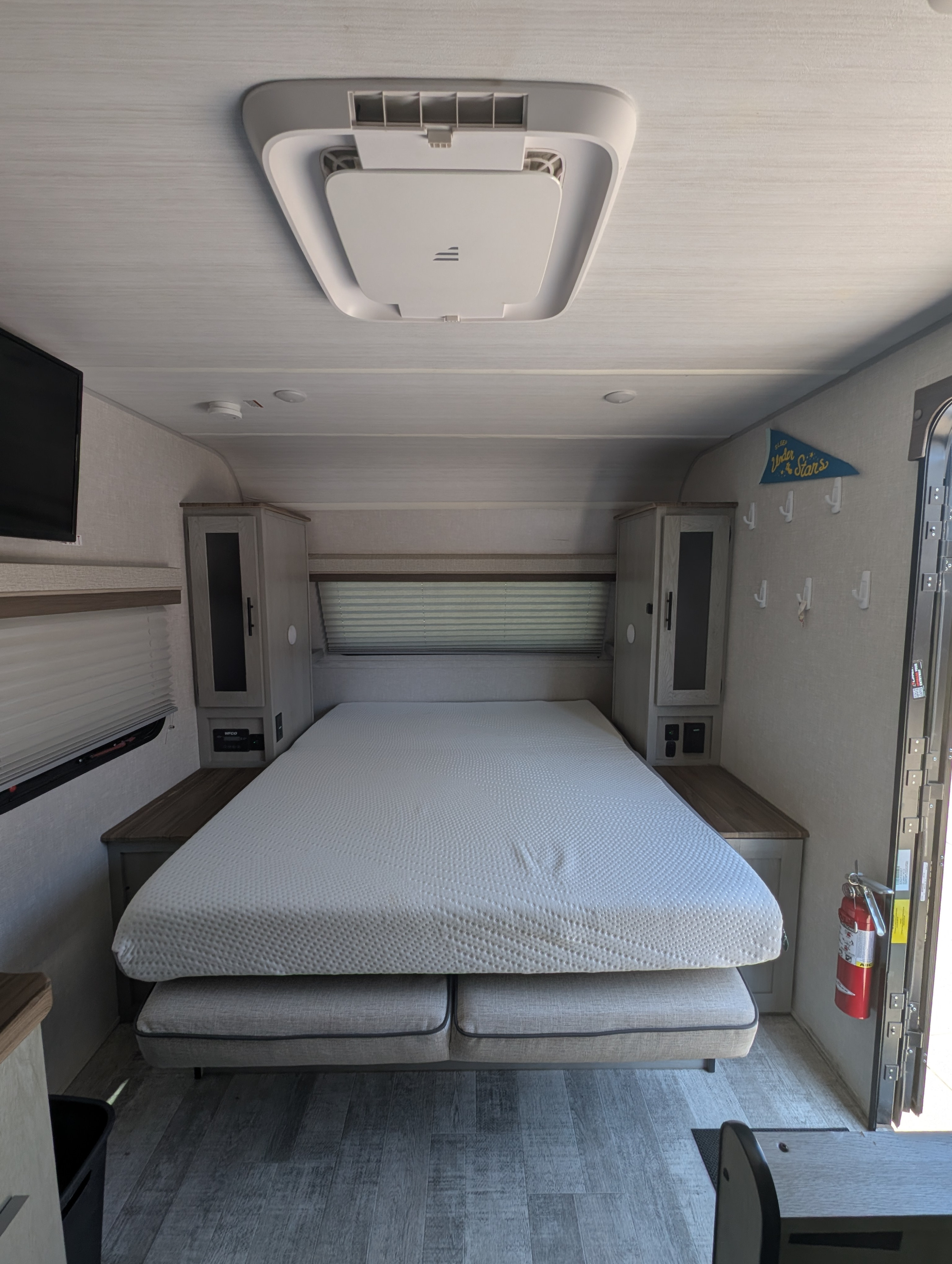 This rv rental features a cozy bedroom with a convertible bed, overhead AC, storage, and a fire extinguisher near the door.. Forest River Ibex 2023