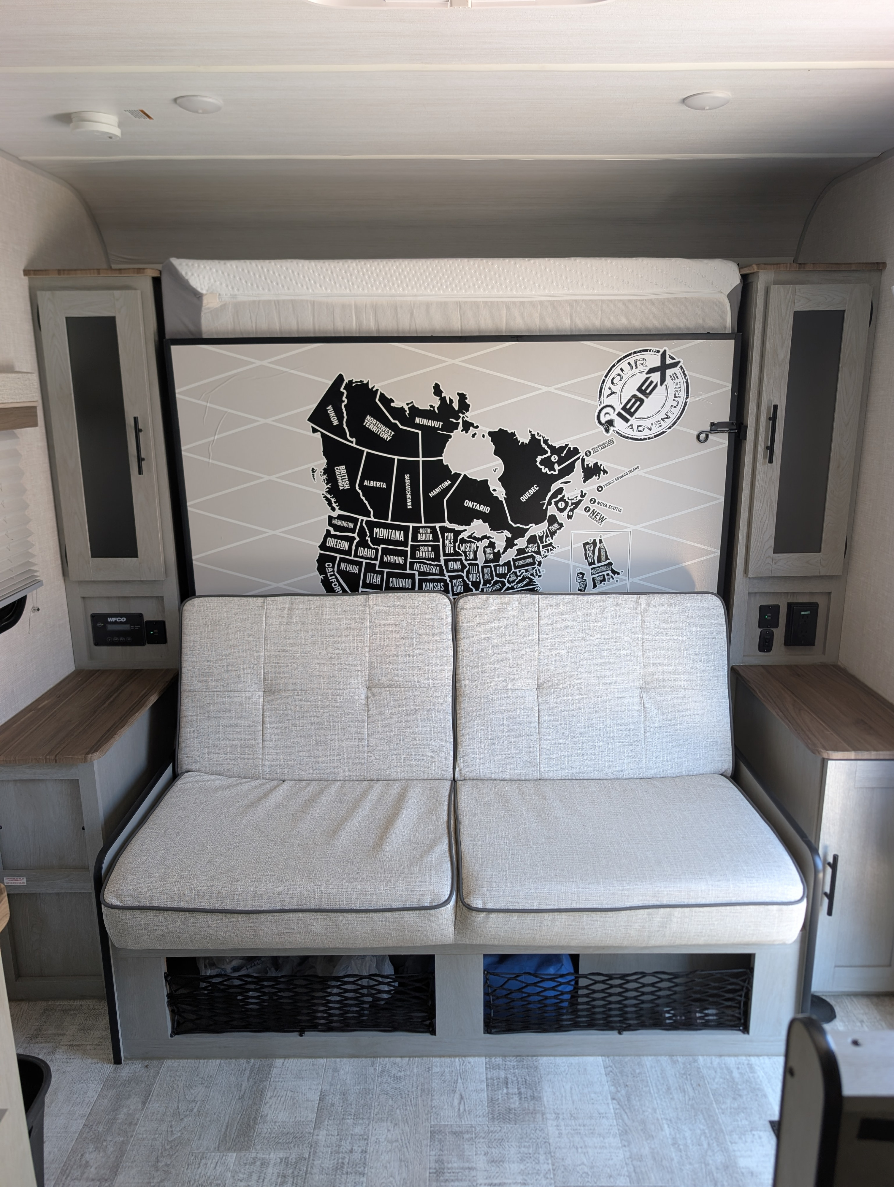RV rental interior: sofa and hidden bed area with under-seat storage, side cabinets, and a North American travel map decor.. Forest River Ibex 2023