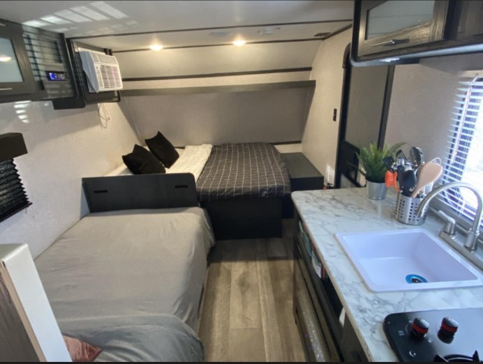 Cozy RV rental interior with beds, a small kitchen with sink & stovetop, and an AC unit, ideal for travel comfort.. Aspen Trail LE 2022