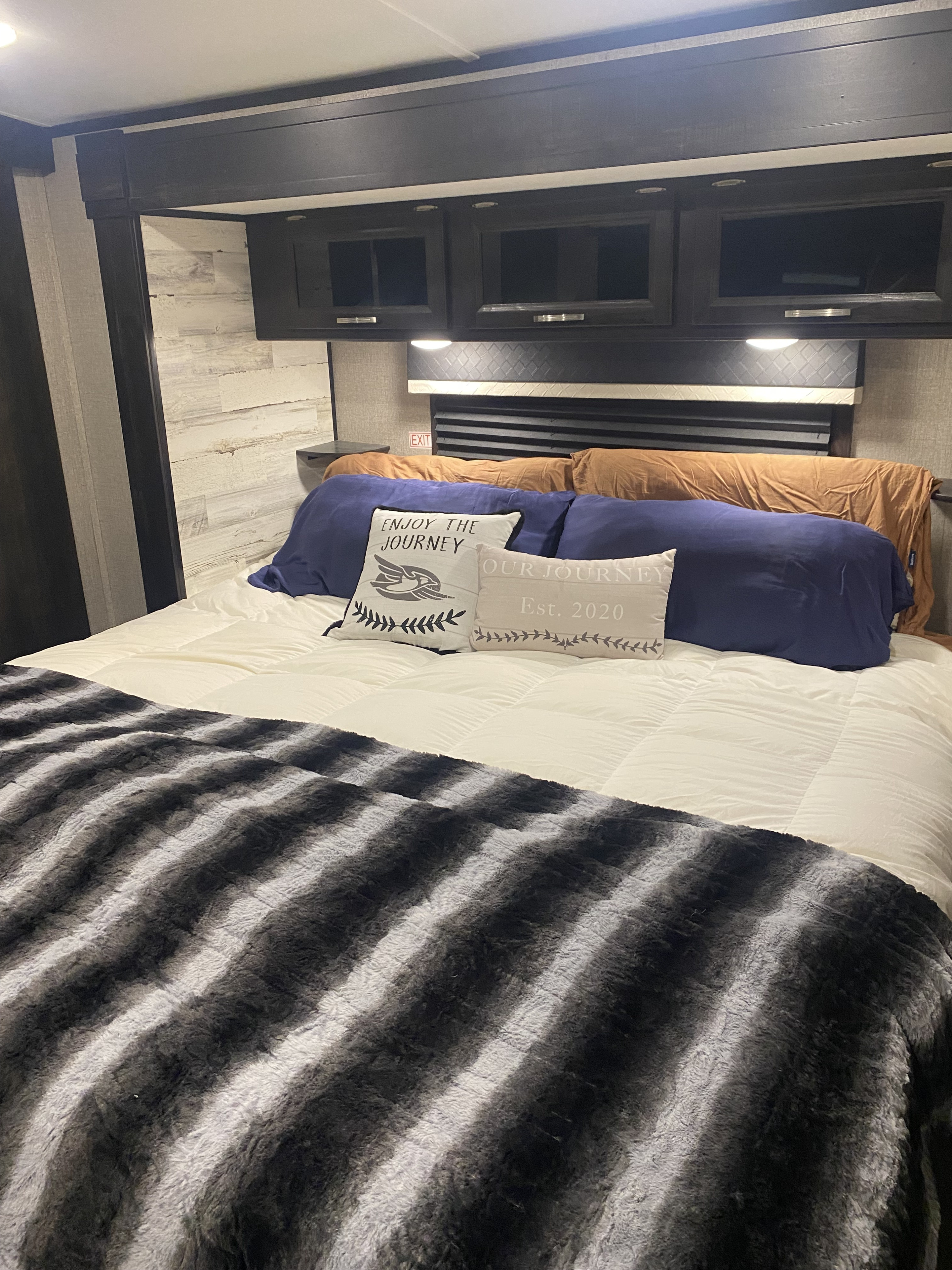 Comfortable RV rental bedroom with a plush bed, navy pillows, a striped blanket, and dark overhead storage cabinets.. Jayco White Hawk 2020
