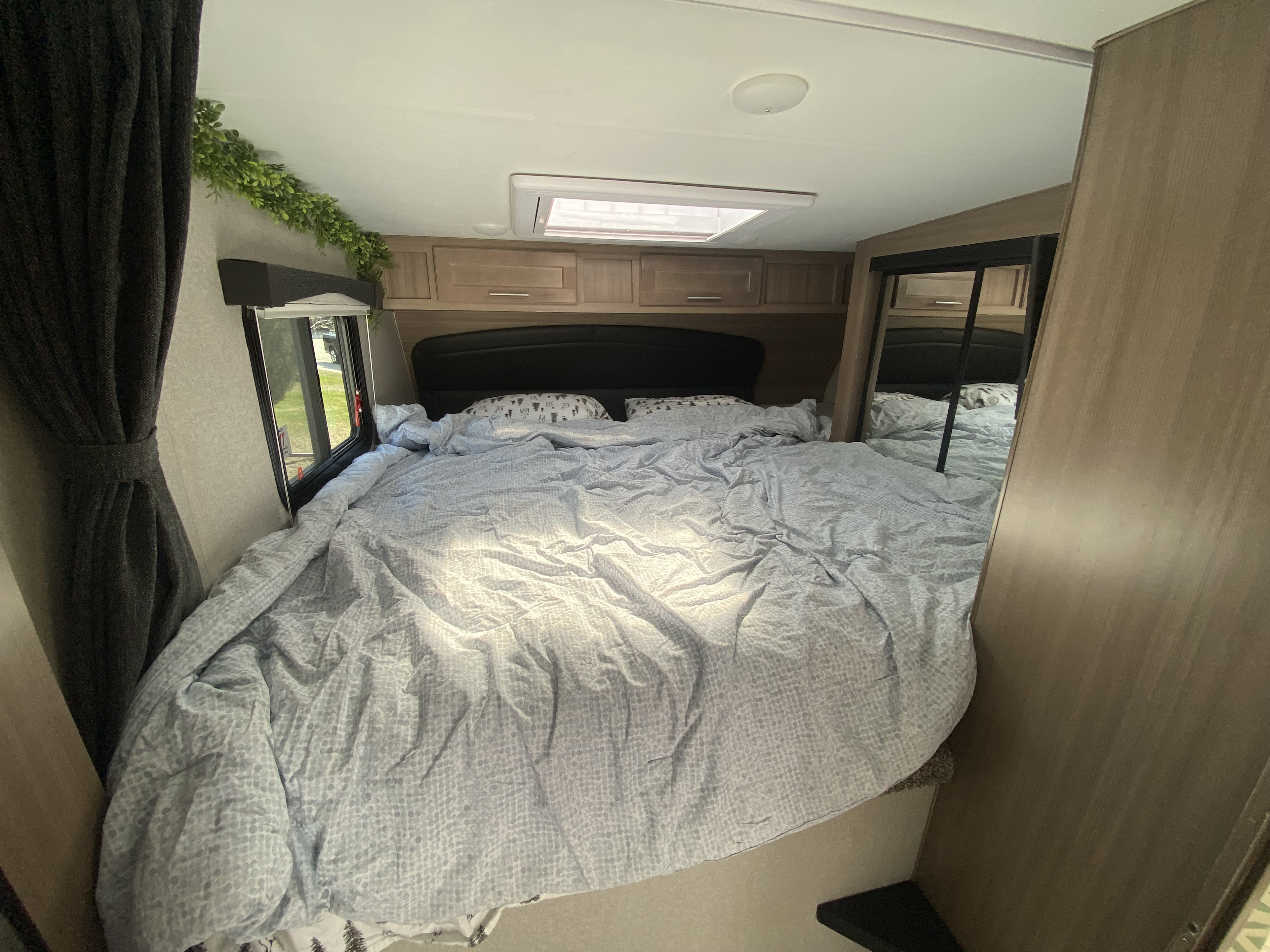 Unmade bed in a compact RV rental bedroom, featuring windows, cupboards, a mirror, and an overhead skylight.. Ford Ford F-350 2020