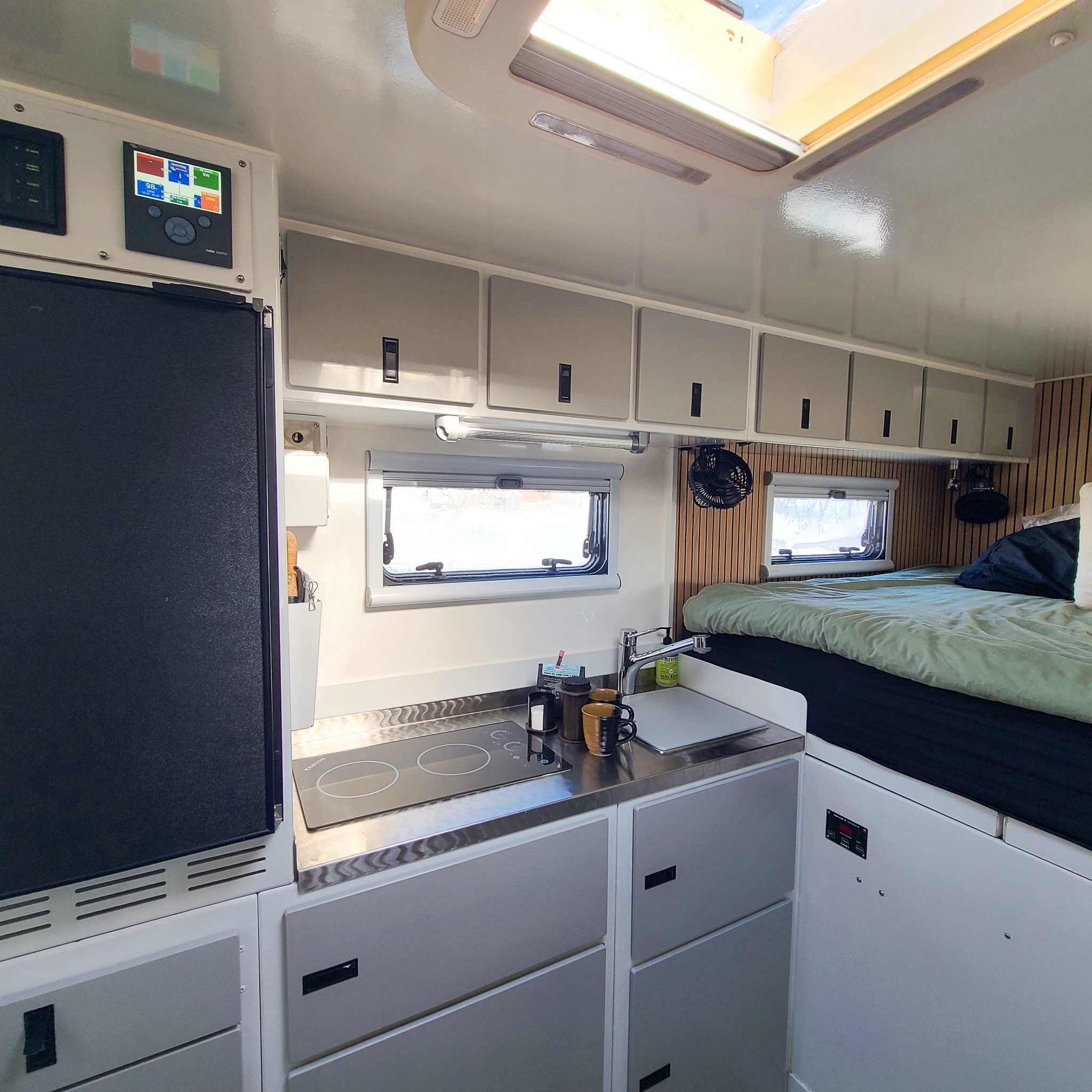 This modern rv rental interior features a compact kitchenette with an induction cooktop, fridge, and cozy bedroom area.. Acela Monterra 2018