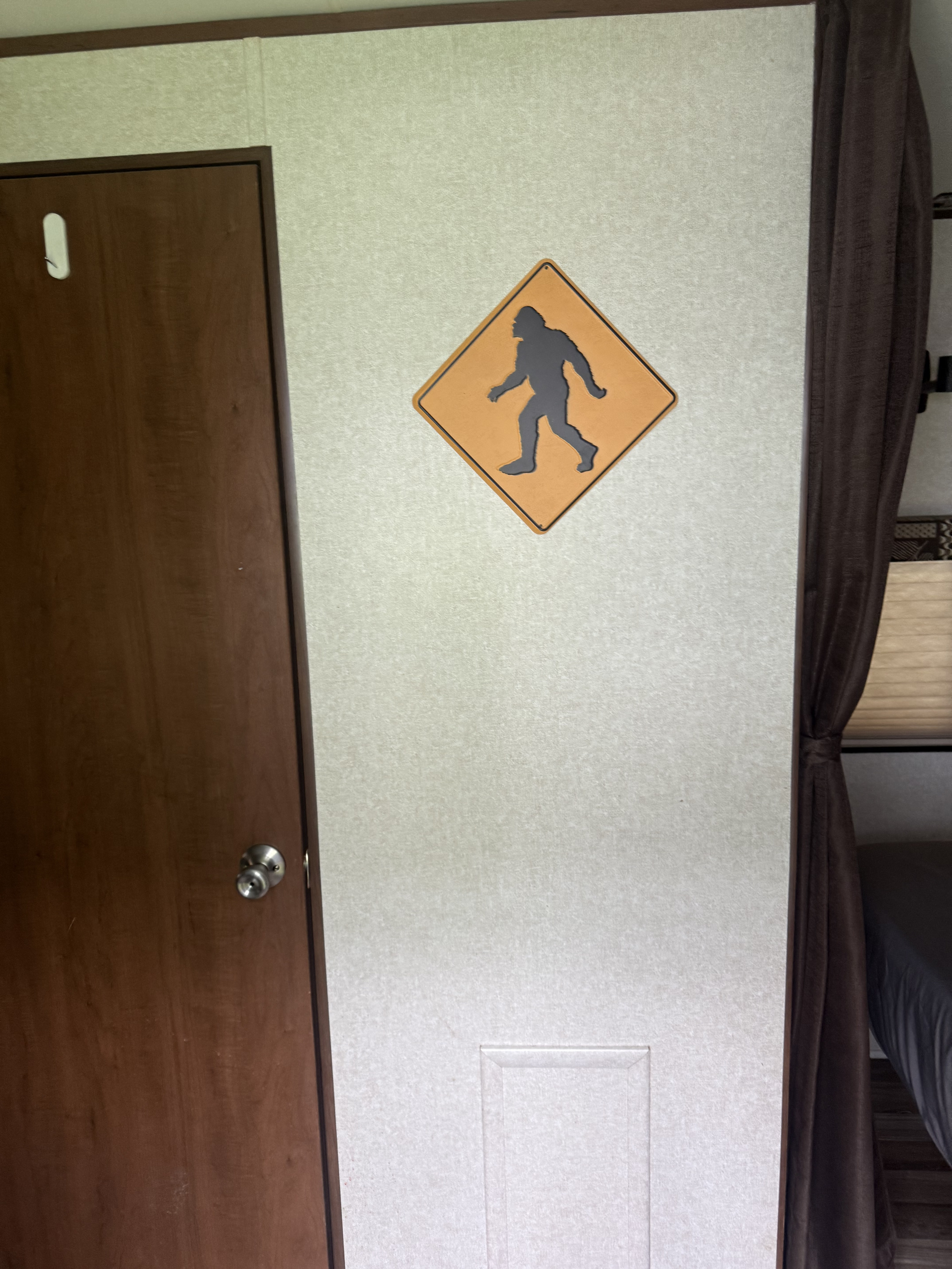 Orange Bigfoot crossing sign on a light wall inside an RV rental, next to a brown door and dark curtain.. Jayco Jay Flight 2017