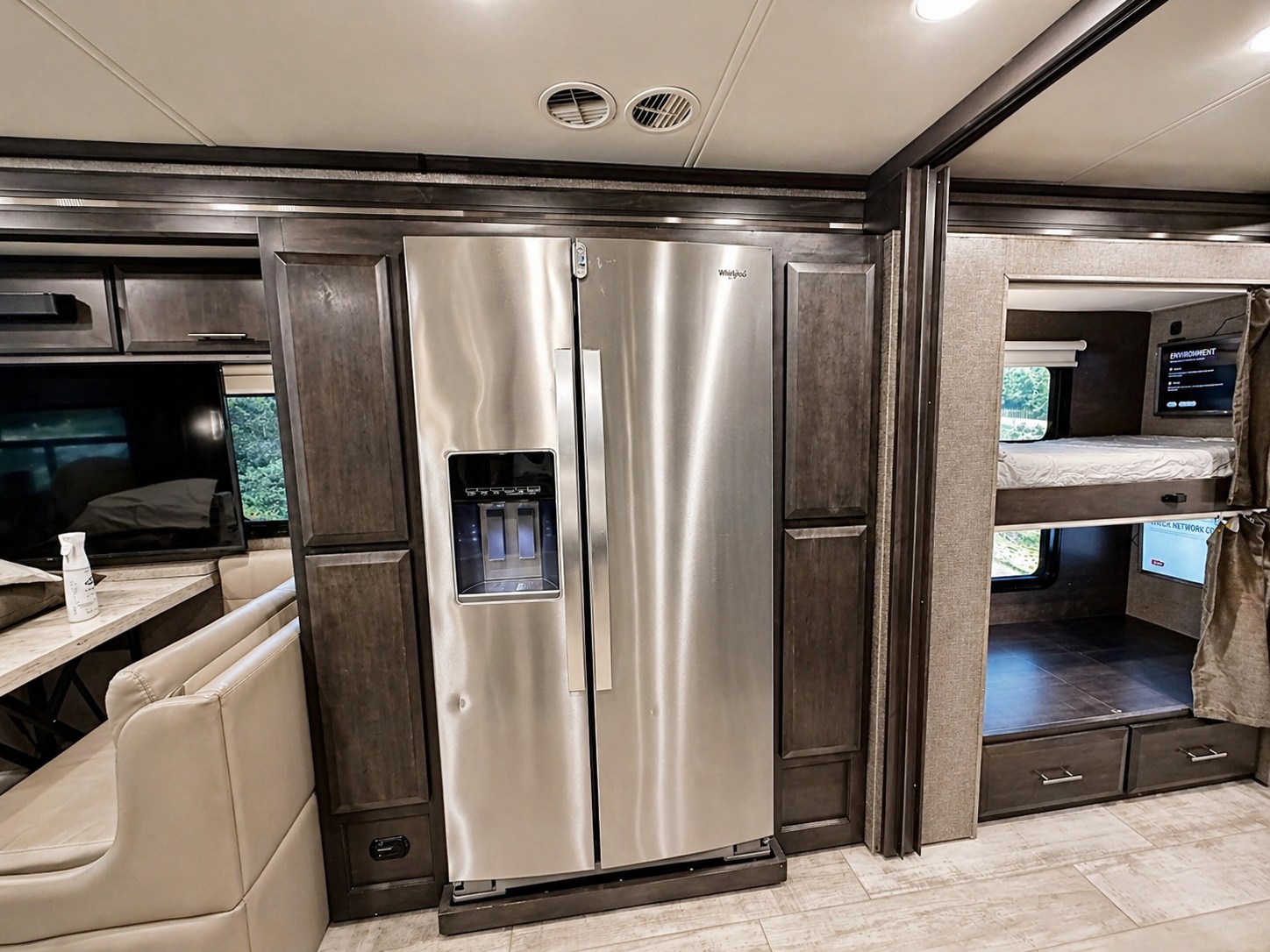 RV rental interior featuring a large stainless steel fridge, bunk beds with individual TVs, and a cozy dining area.. Thor Venitian 2021