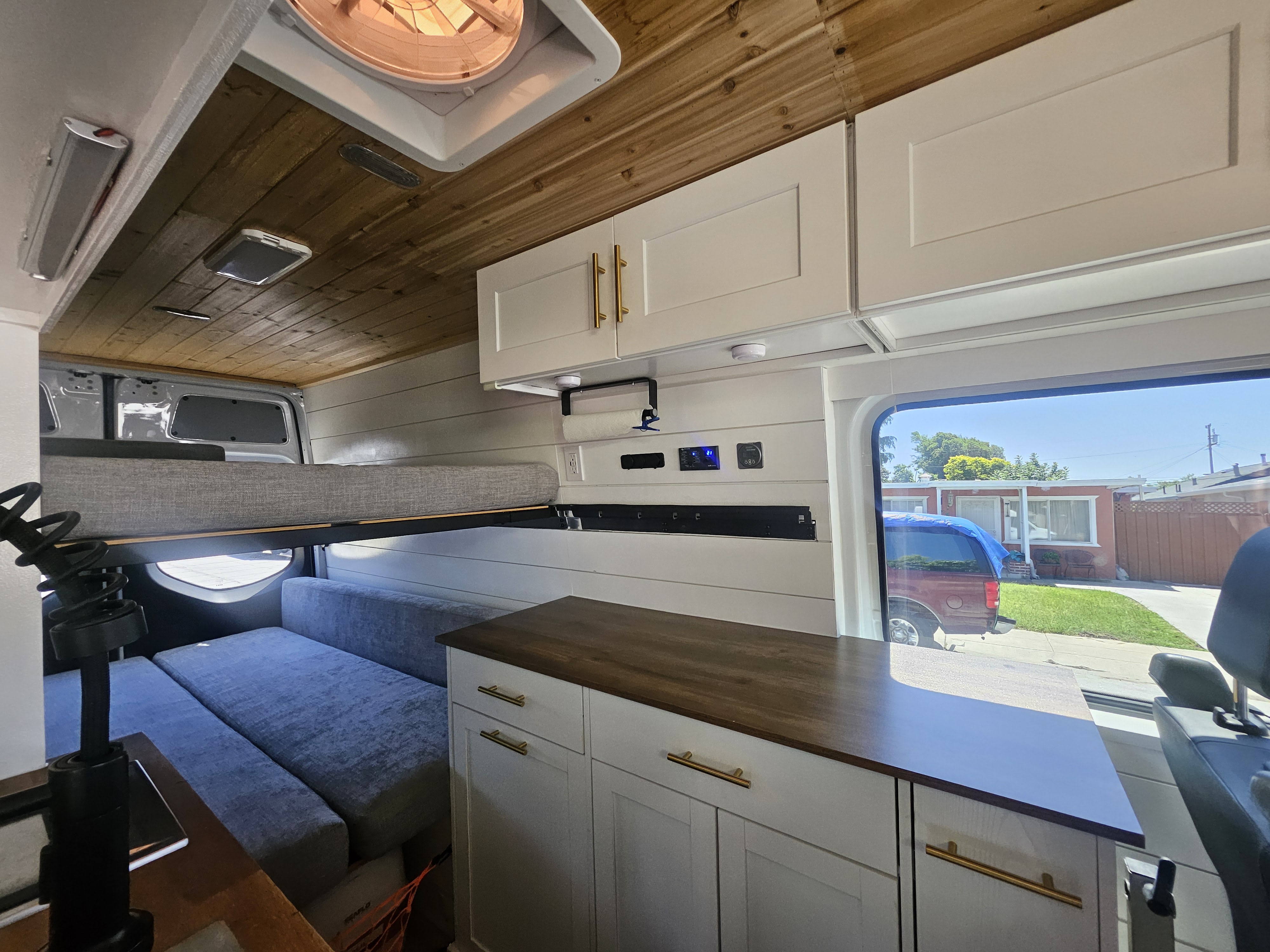 Spacious and modern RV rental interior with a wooden ceiling, white cabinets, and cozy sleeping/seating areas.. Mercedes Benz Sprinter 2020