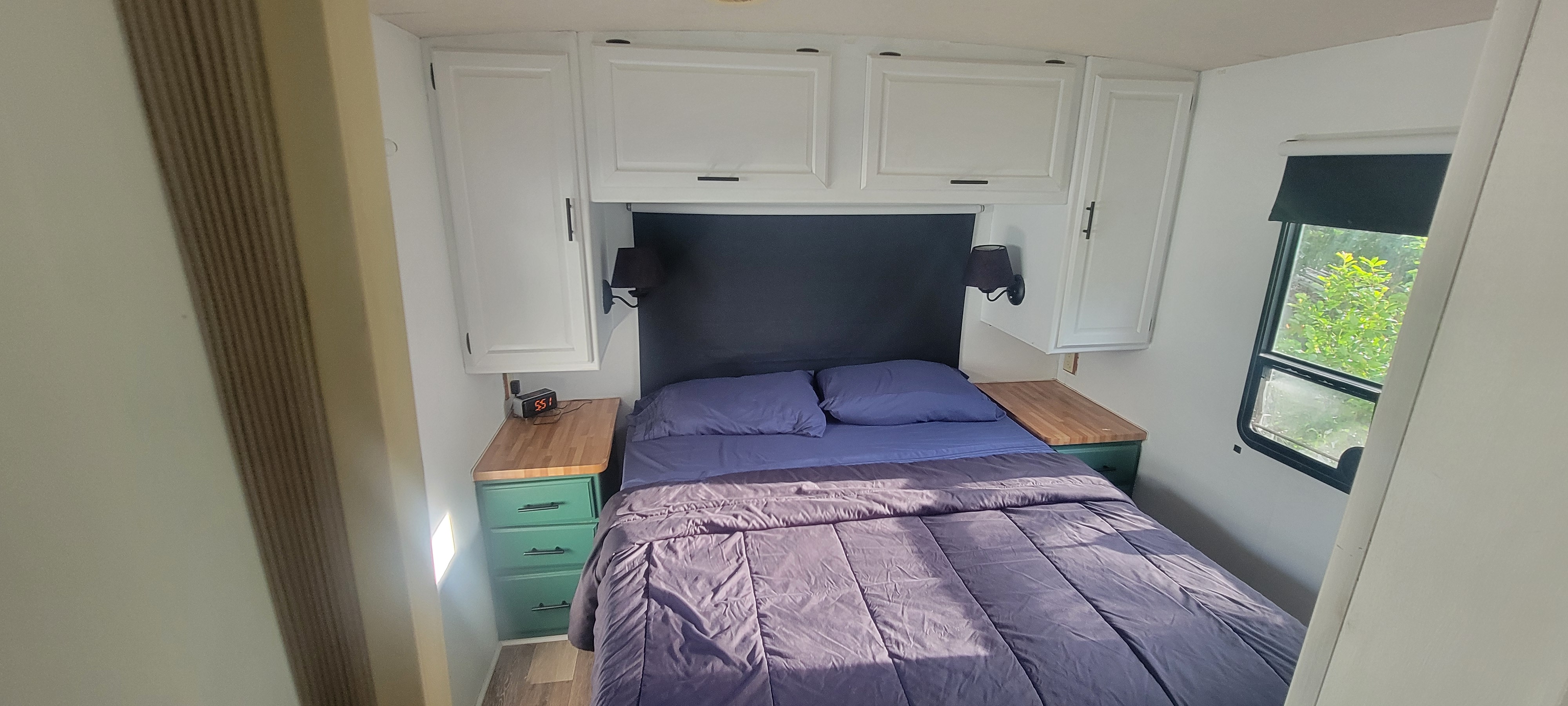 Modern RV rental bedroom with white cabinetry, green nightstands, and a cozy bed, featuring a window and ample storage.. Winnebago Brave 1997
