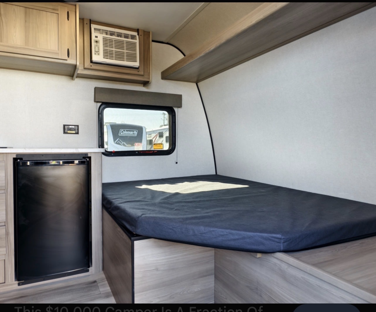 Compact rv rental interior featuring a comfortable bed, small refrigerator, AC unit, overhead cabinets, and a window.. Keystone RV 13b 2026