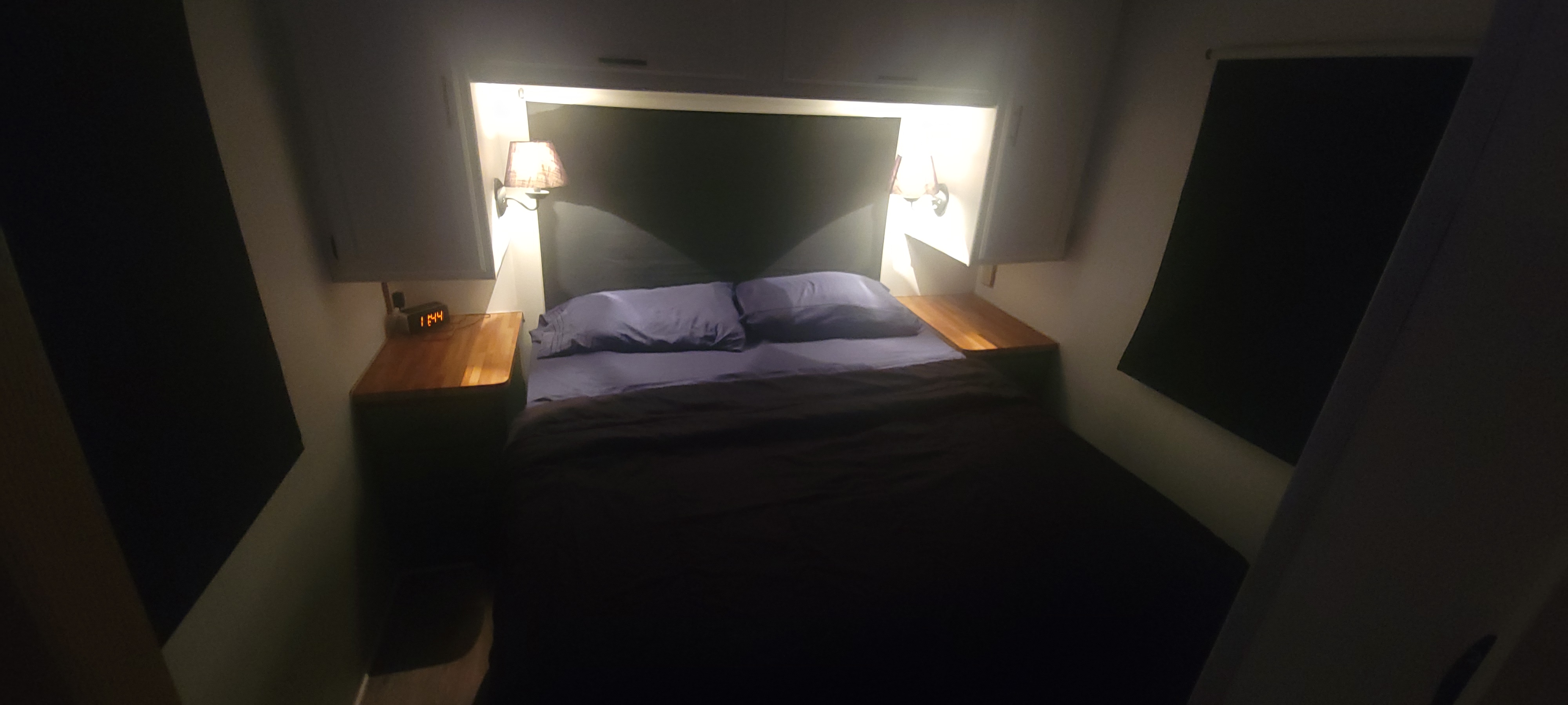 Cozy RV rental bedroom with bed, nightstands, two lamps, and an alarm clock displaying 1:44.. Winnebago Brave 1997
